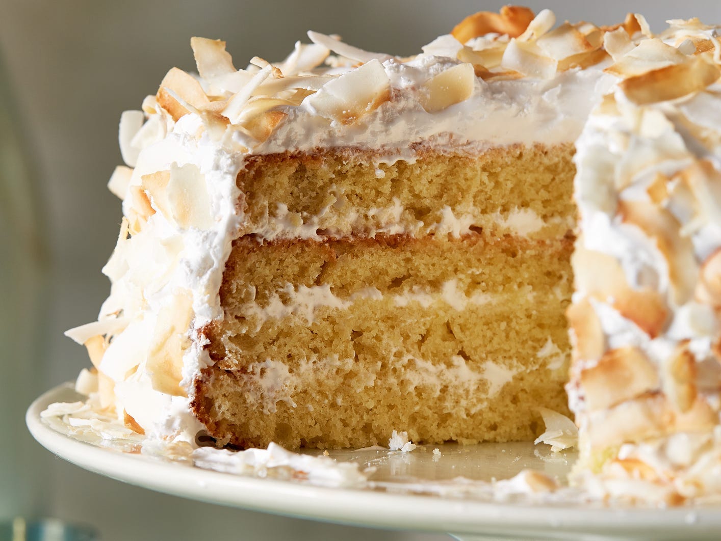 A four-layer coconut cake with a slice taken out revealing the center