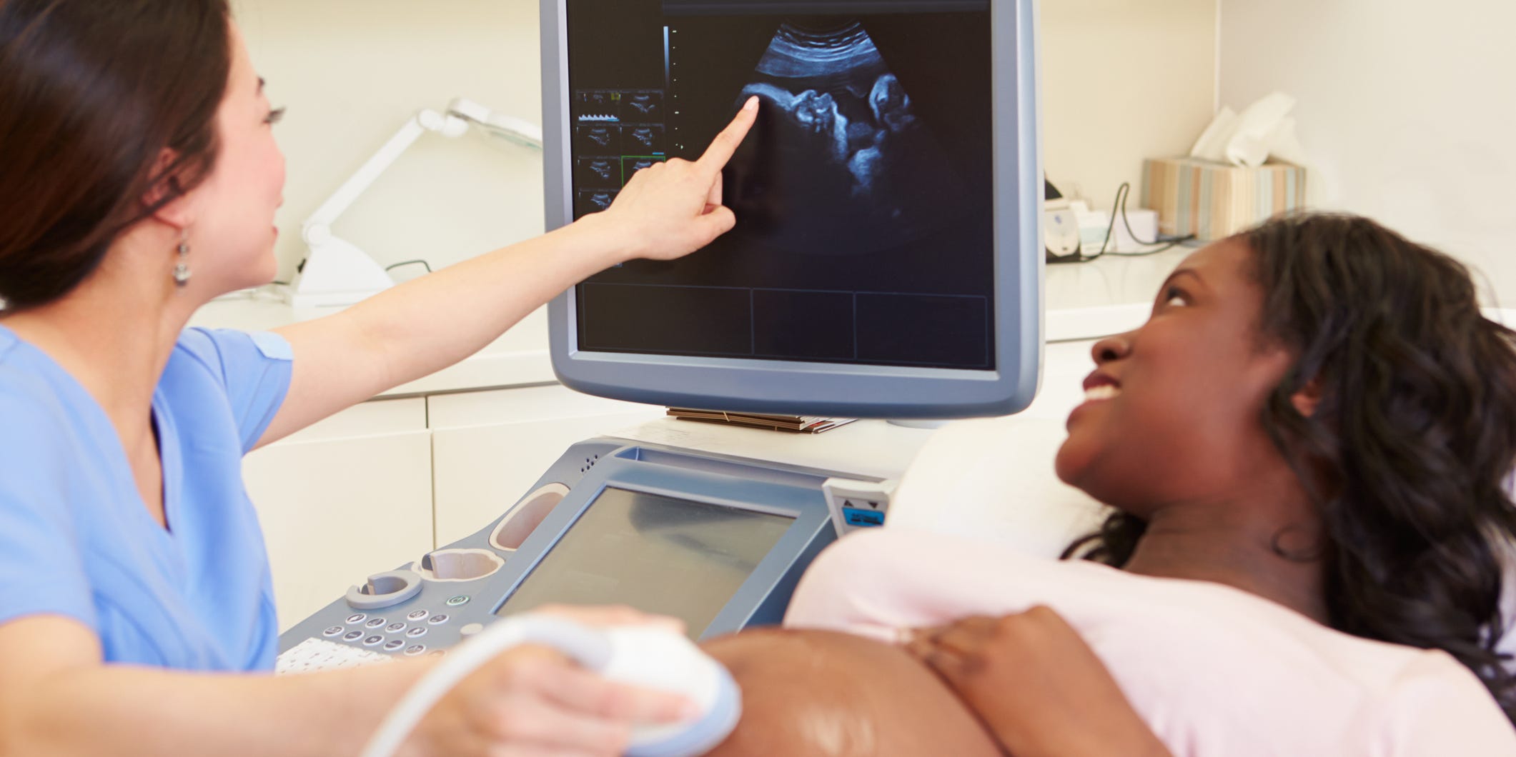 Pregnant woman in 2nd or 3rd trimester getting an ultrasound. Doctor points at the baby's head on a screen.