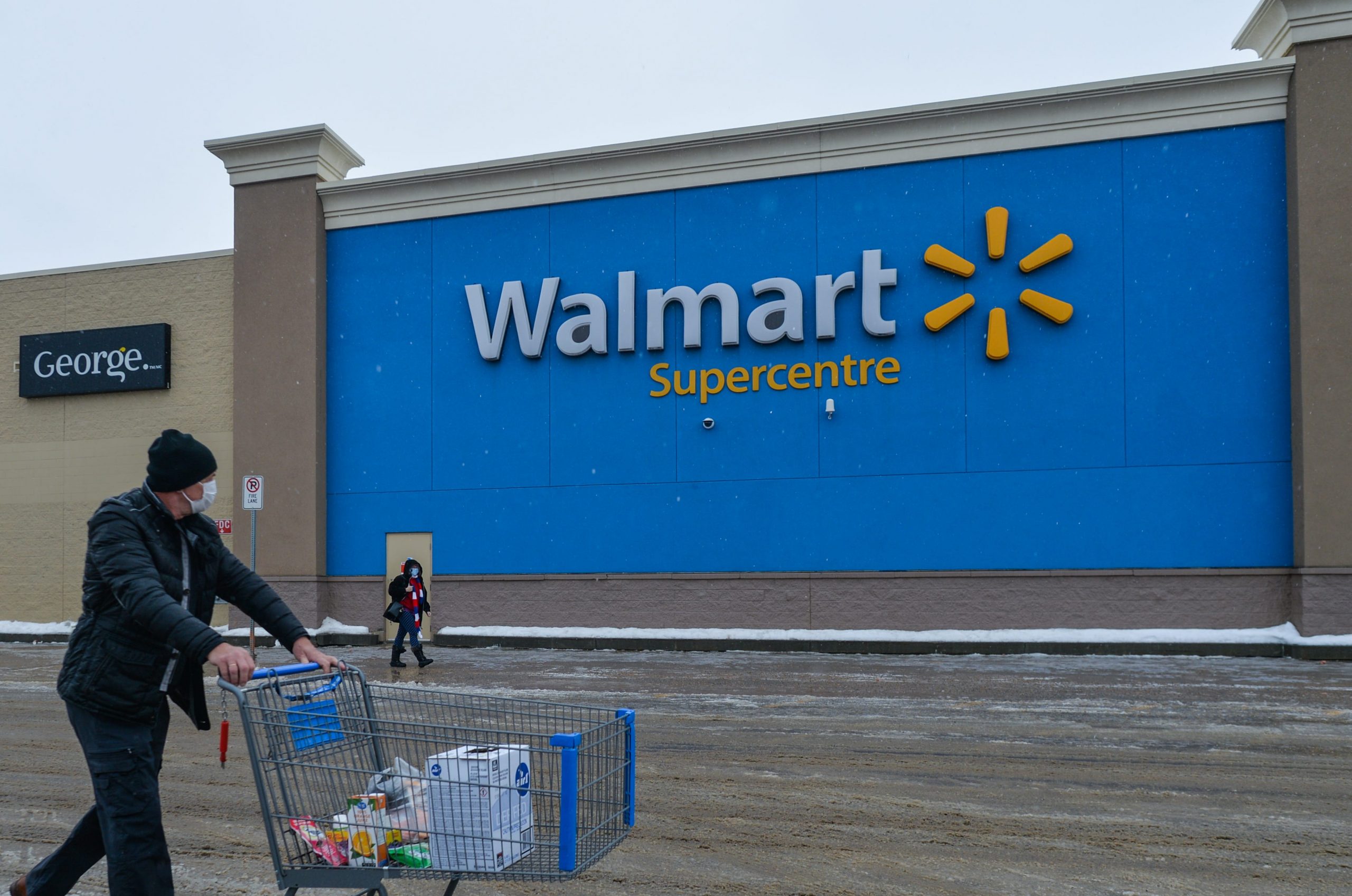 A man wearing a face mask pushes a cart in front of a Walmart