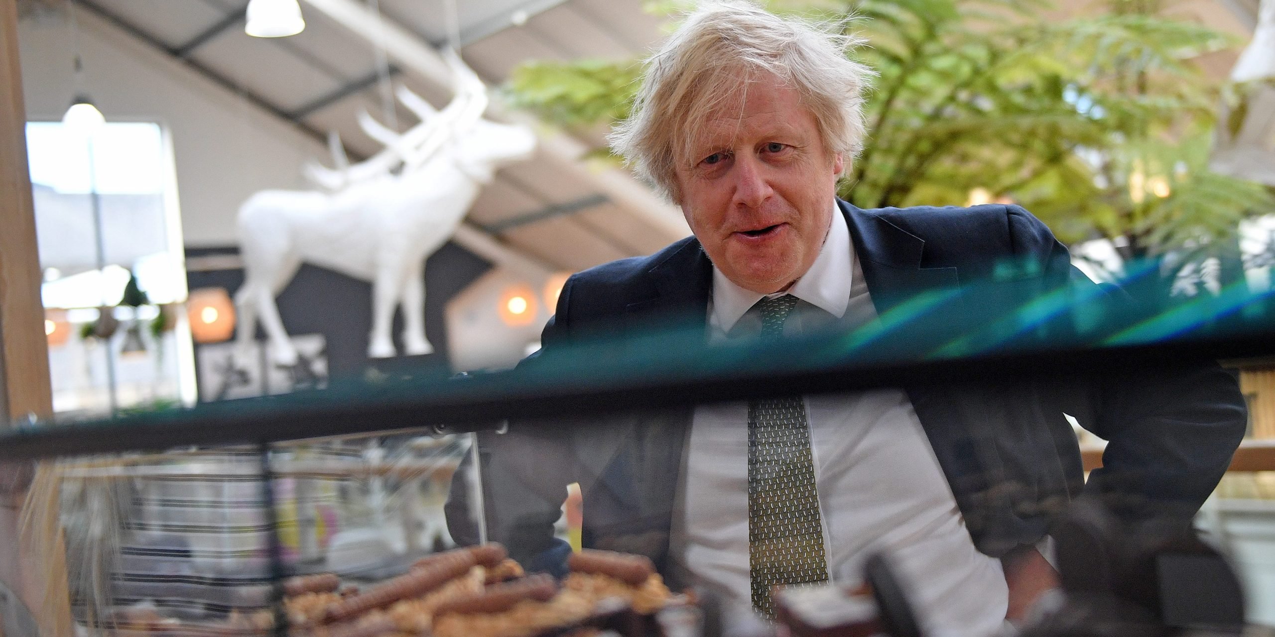 British Prime Minister Boris Johnson reacts as he looks at a display of cakes and desserts as he talks with business owners inside Lemon Street Market on April 7, 2021 in Truro, England.