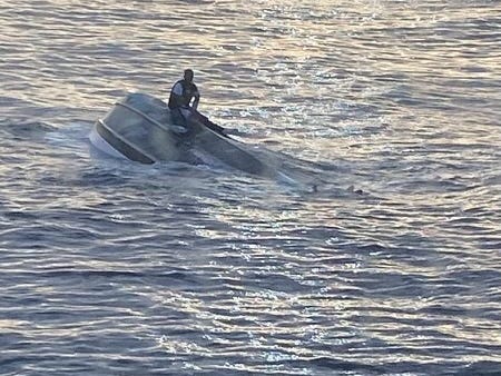 An unidentified survivor sits on top of an overturned boat in the middle of the ocean