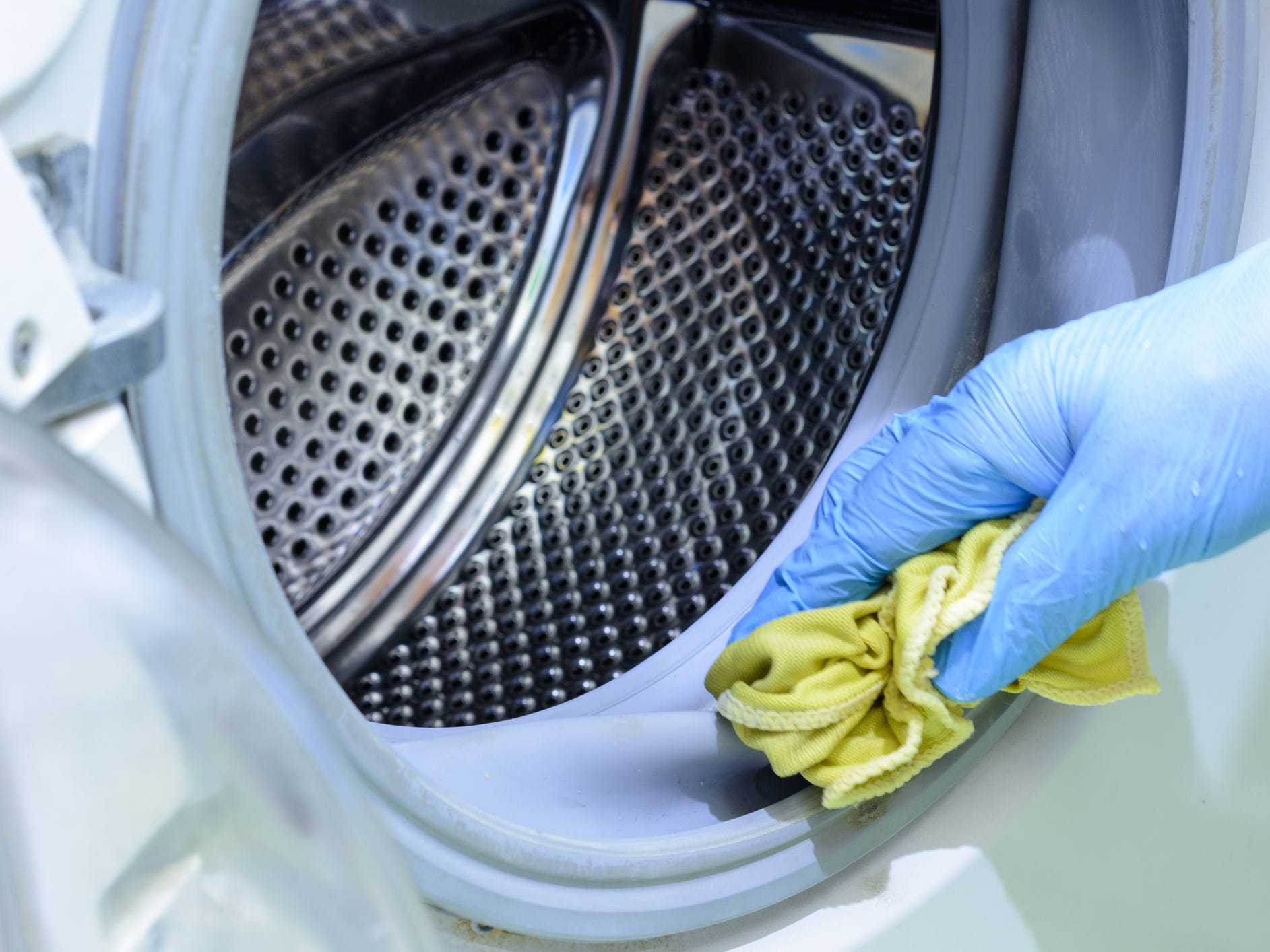 A hand wearing a blue rubber glove using a yellow cloth to clean a washing machine