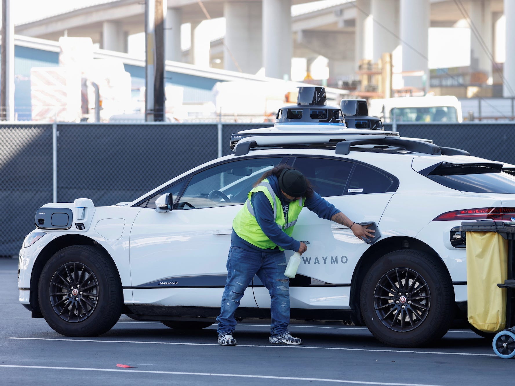 A guy in yellow vest appears to be cleaning a white Waymo self-driving car