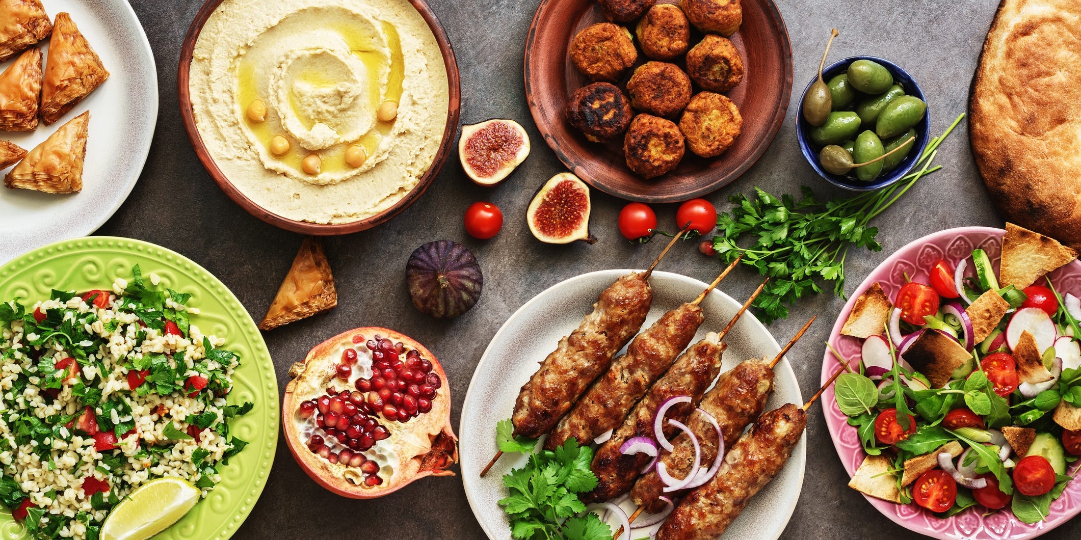 Various plates of Mediterranean/Middle Eastern food including hummus, falafel, tabbouleh, salad, and baklava.