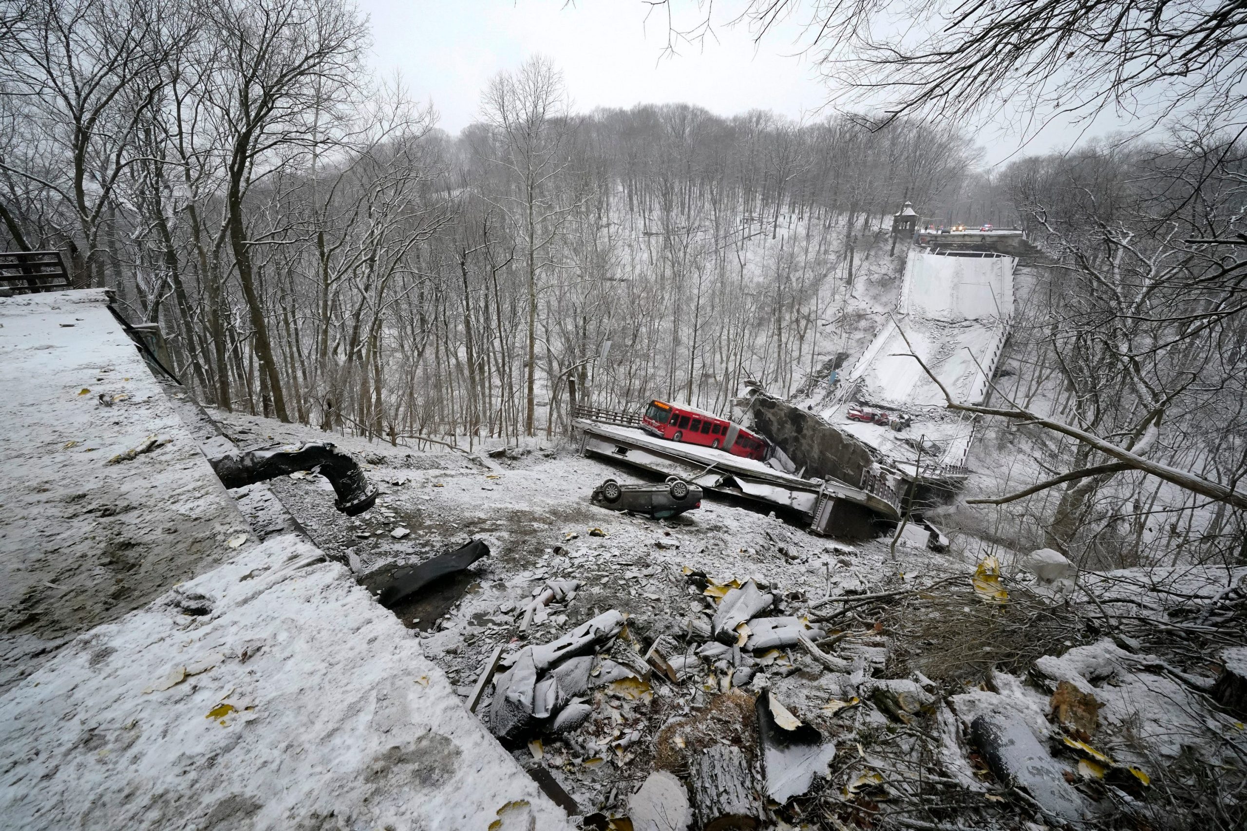 scene of pittsburgh bridge collapse shows red bus at the bottom of a snow-covered ravine