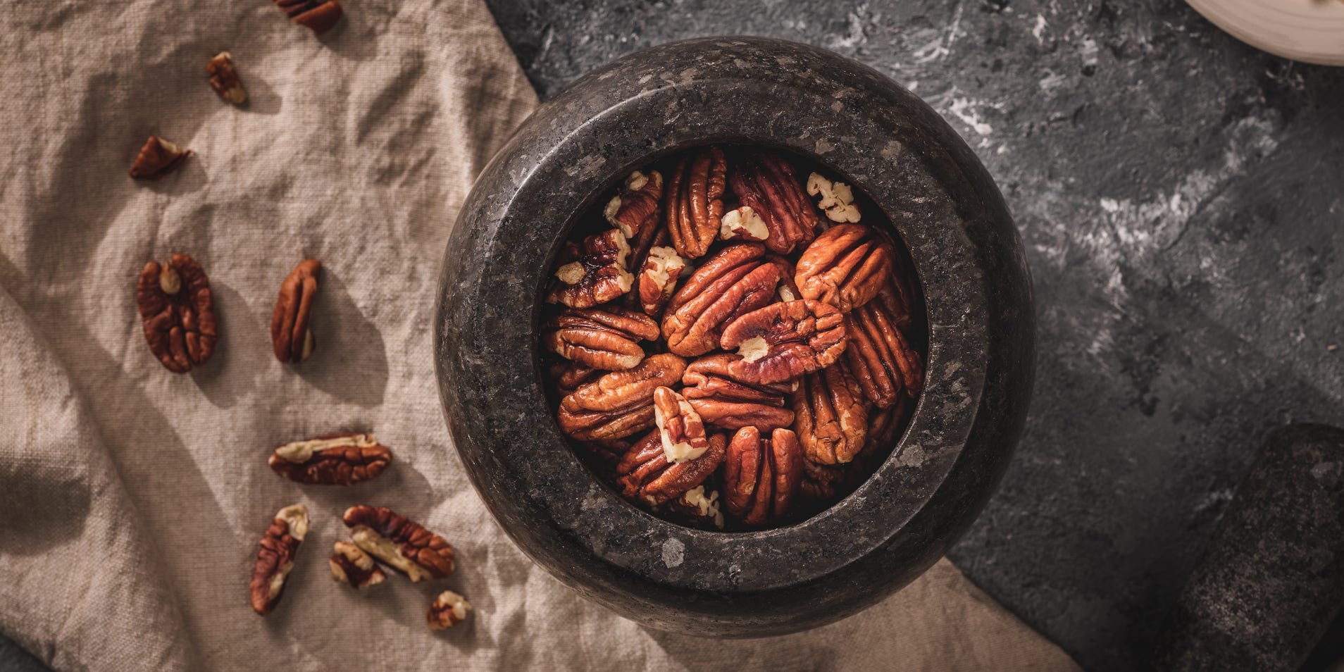 Toasted pecans in a mortar and pestle with some light styling in the background