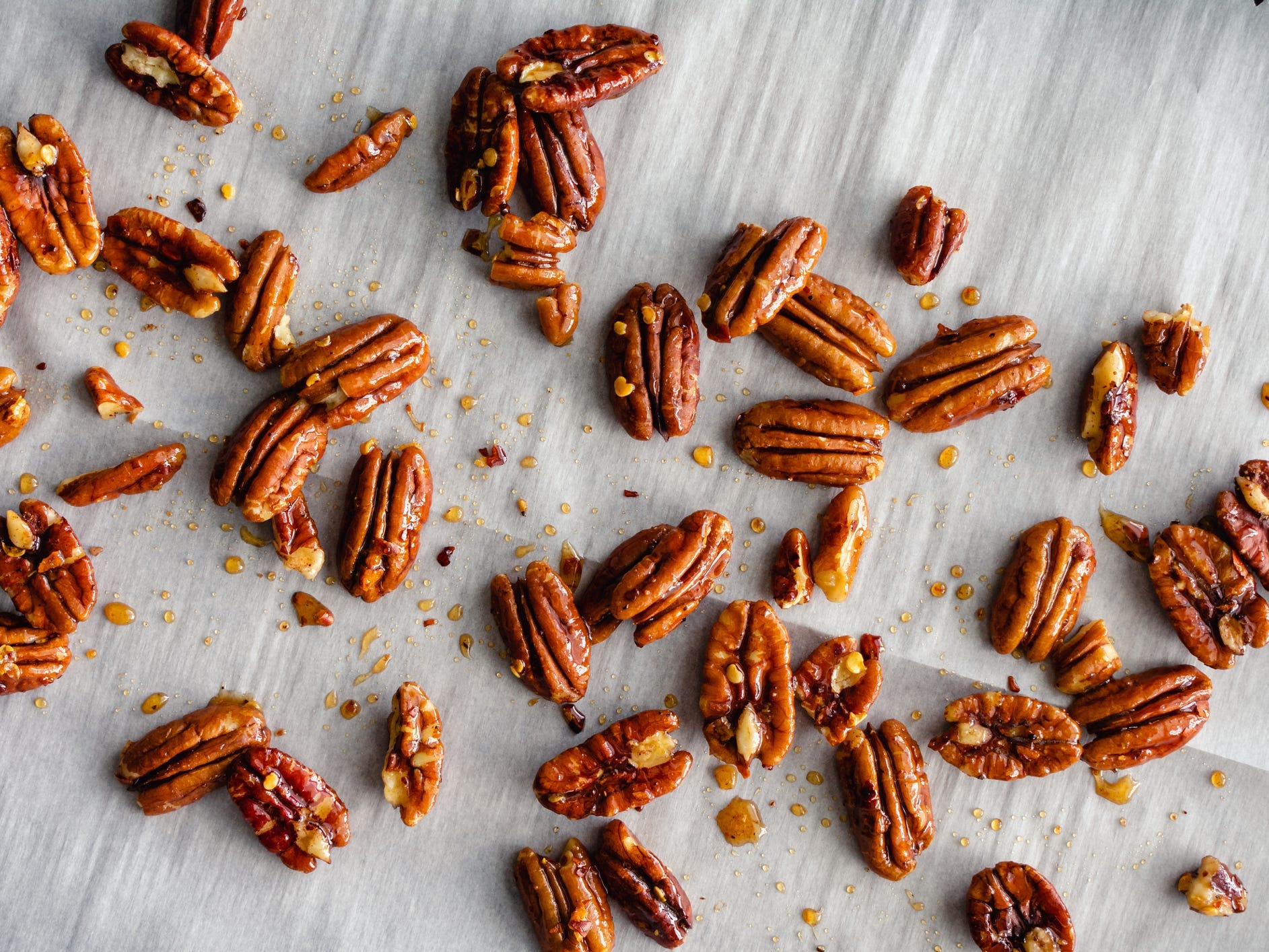 Candied pecans spaced out on a sheet tray with parchment.