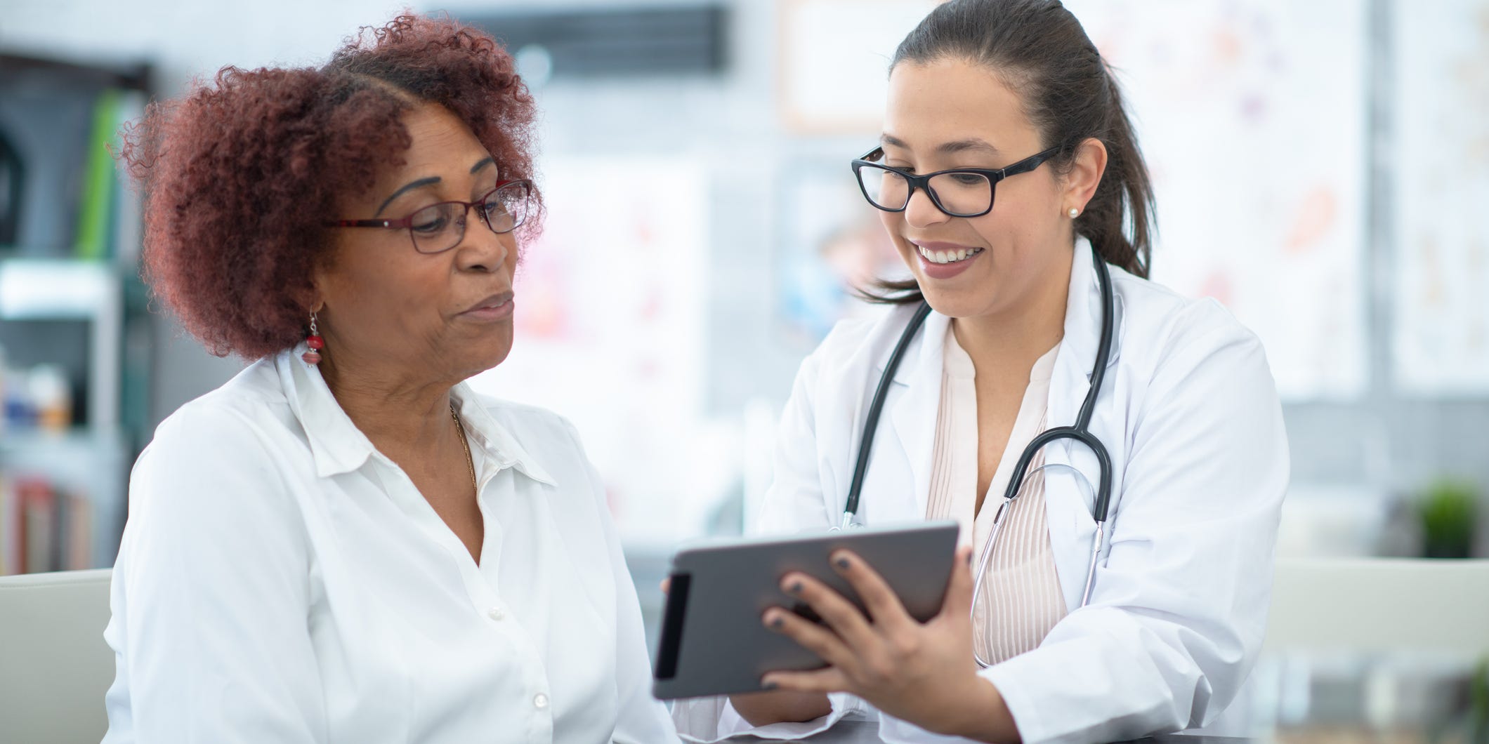 Doctor and mature adult woman look at medical records or results together on a tablet.