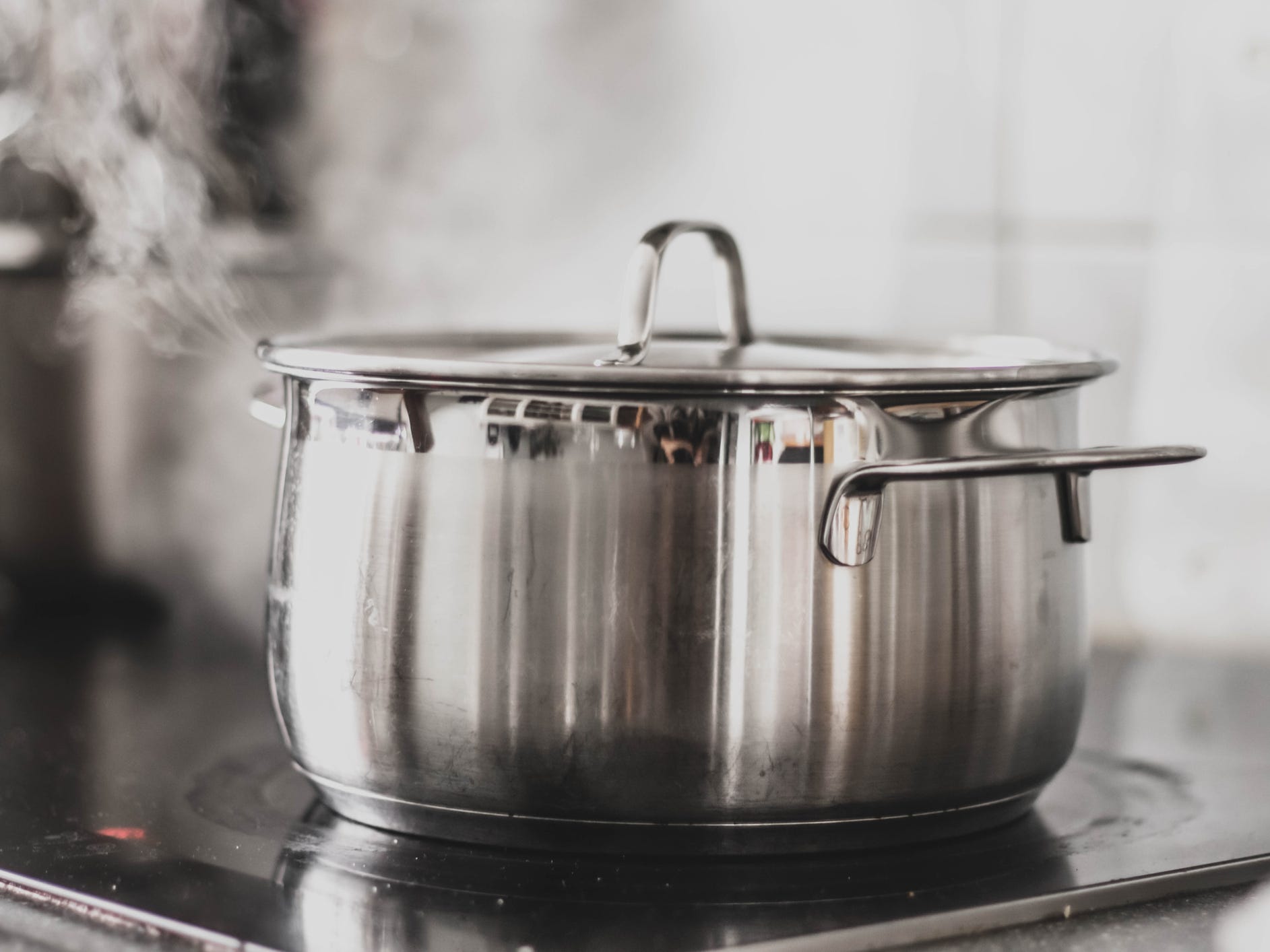 A pot on a stove covered with a metal lid with steam coming out