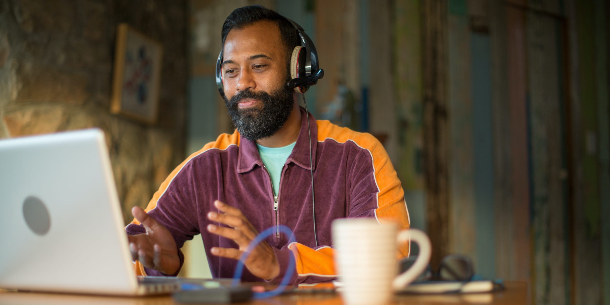 man speaking into laptop computer with headphones on at desk