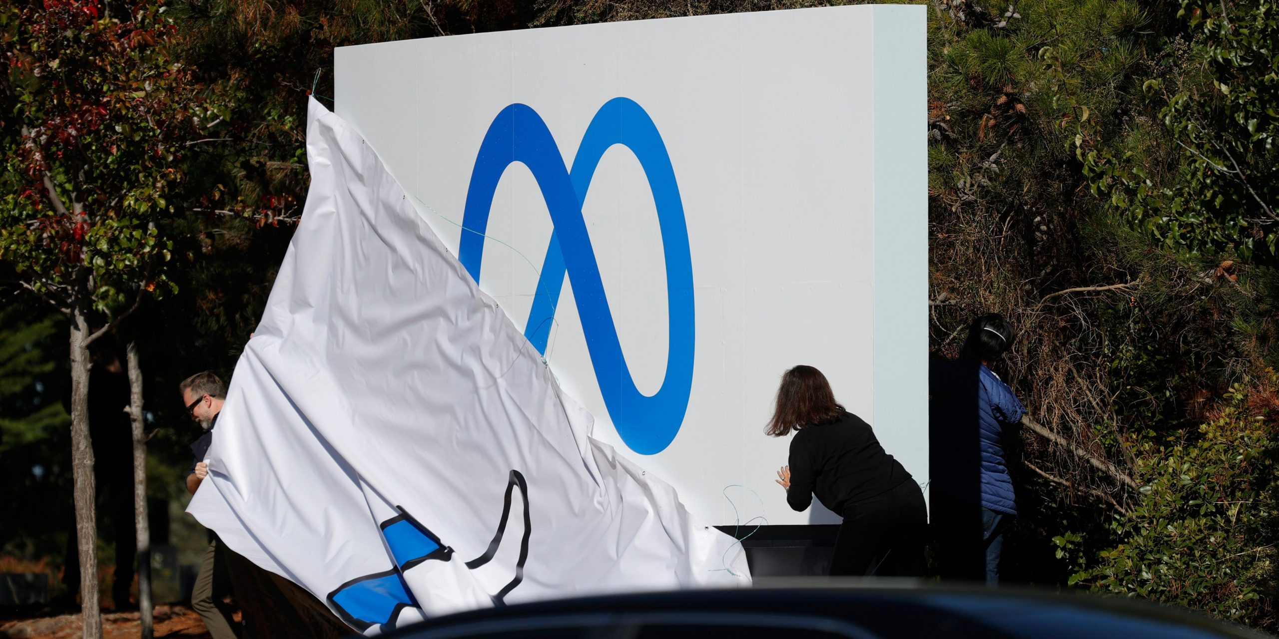 Workers in front of Facebook headquarters pull off cover of the old "thumbs up" sign to reveal the new Meta logo