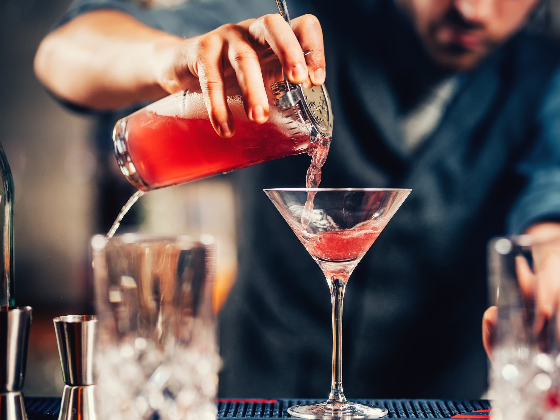 A bartender pouring a cosmopolitan from a shaker into a martini glass