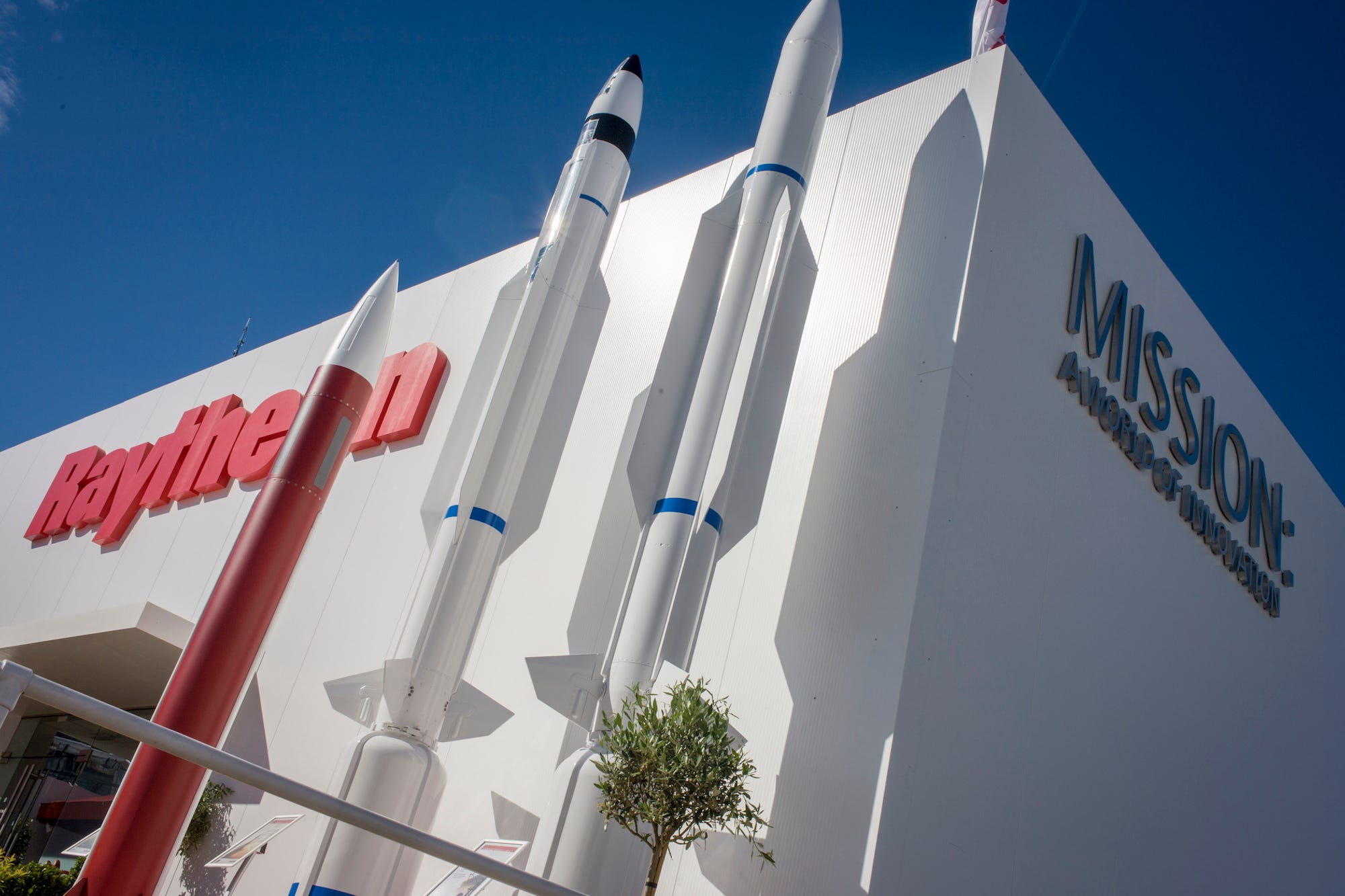 A trio of rockets, one red, one striped, and one plain, adorn the outside of a Raytheon exhibit at an air show in England.