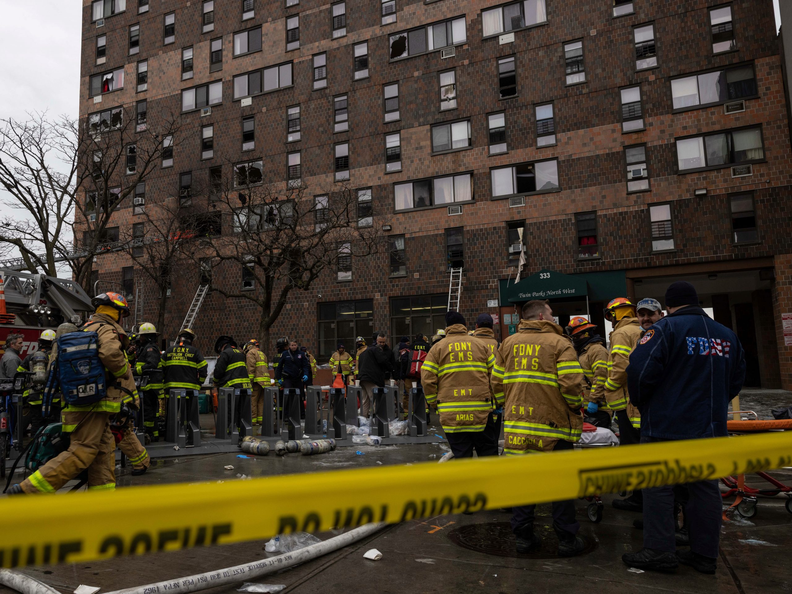 Firefighters stand in front of the Bronx apartment building where a Sunday fire killed 17 people.