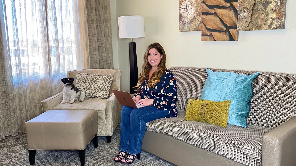 Jill Schildhouse and her dog in their hotel room. Jill has an open laptop on her lap.