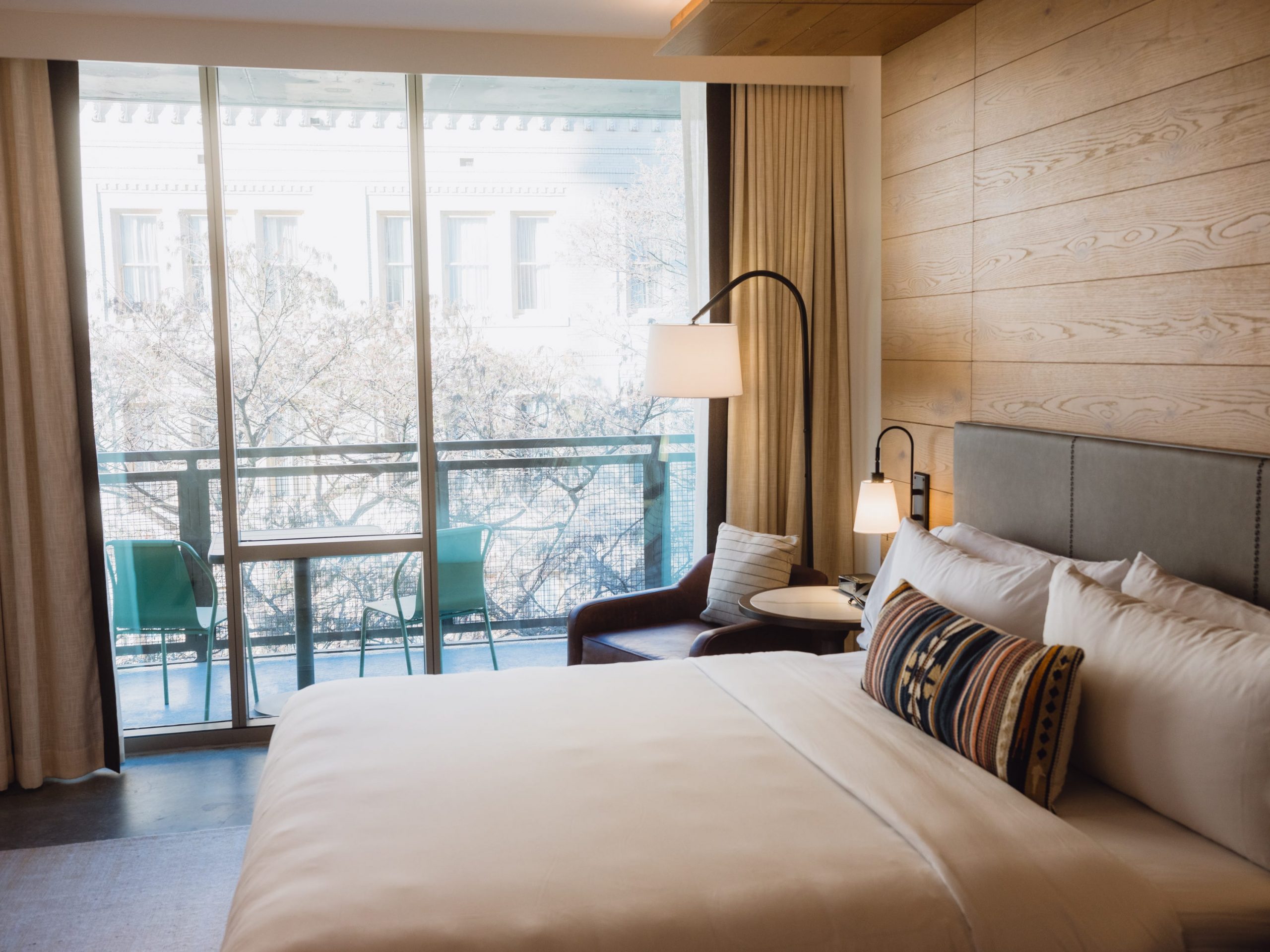 A bed and desk lamp next to a hotel window.