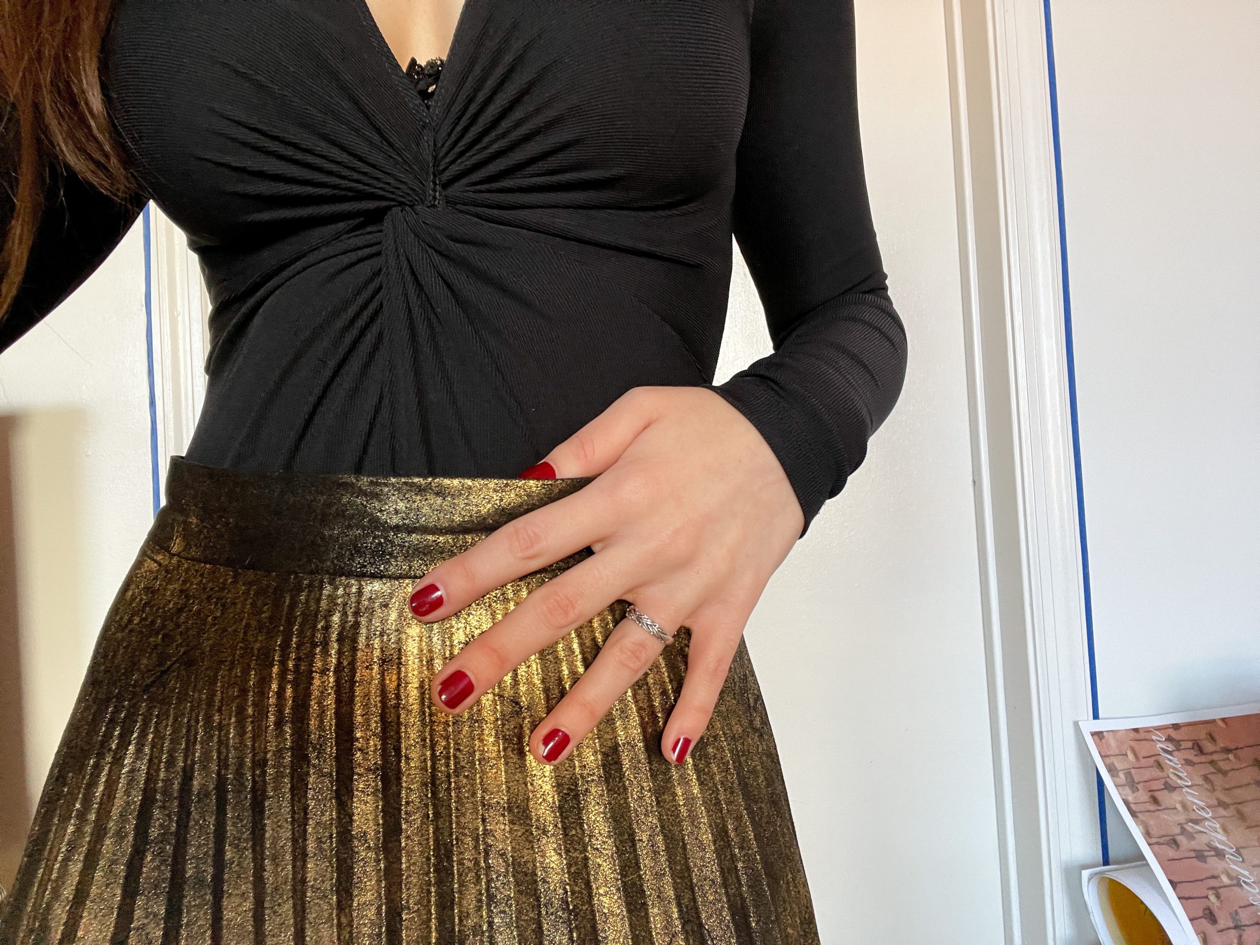 Black wrap top with a gold, knife-pleat skirt and red nail polish