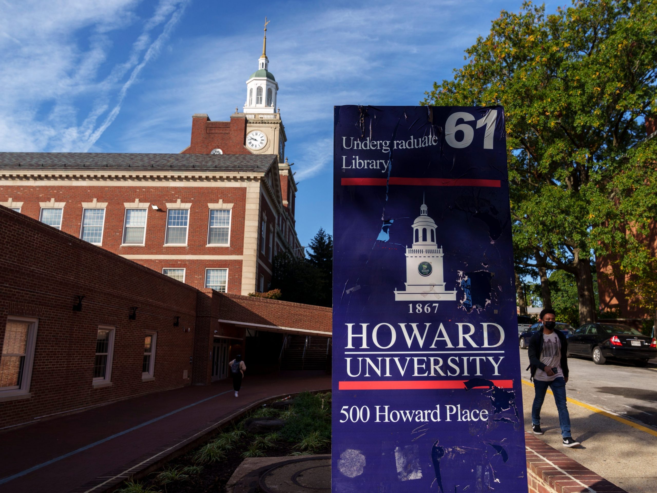 Sign showing 'Howard University' entrance as masked student walks up in the distance.