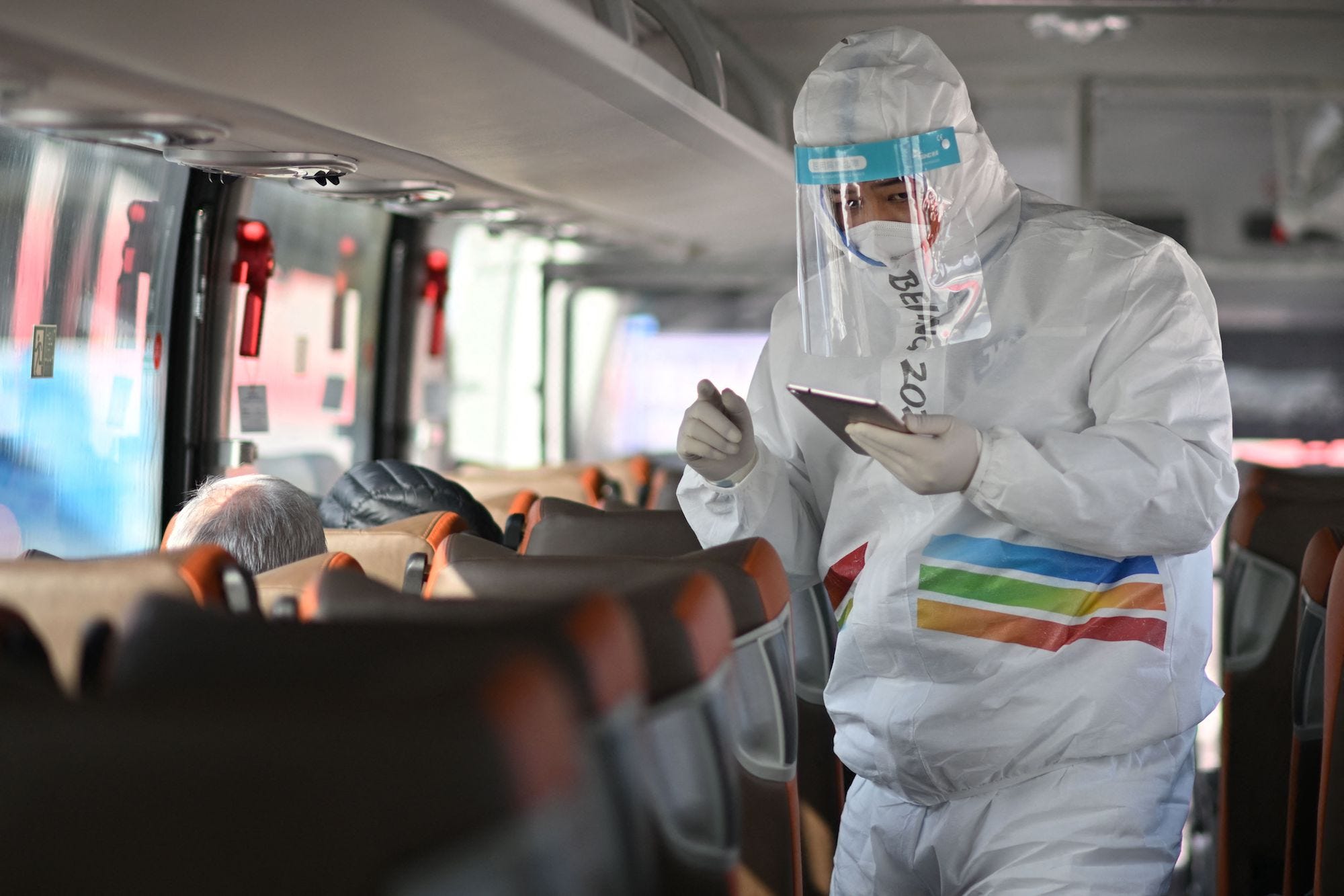 A member of staff wearing a hazmat suit greets media on a bus as they arrive in the Zhangjiakou Zone, east of Beijing ahead of the Beijing 2022 Winter Olympics