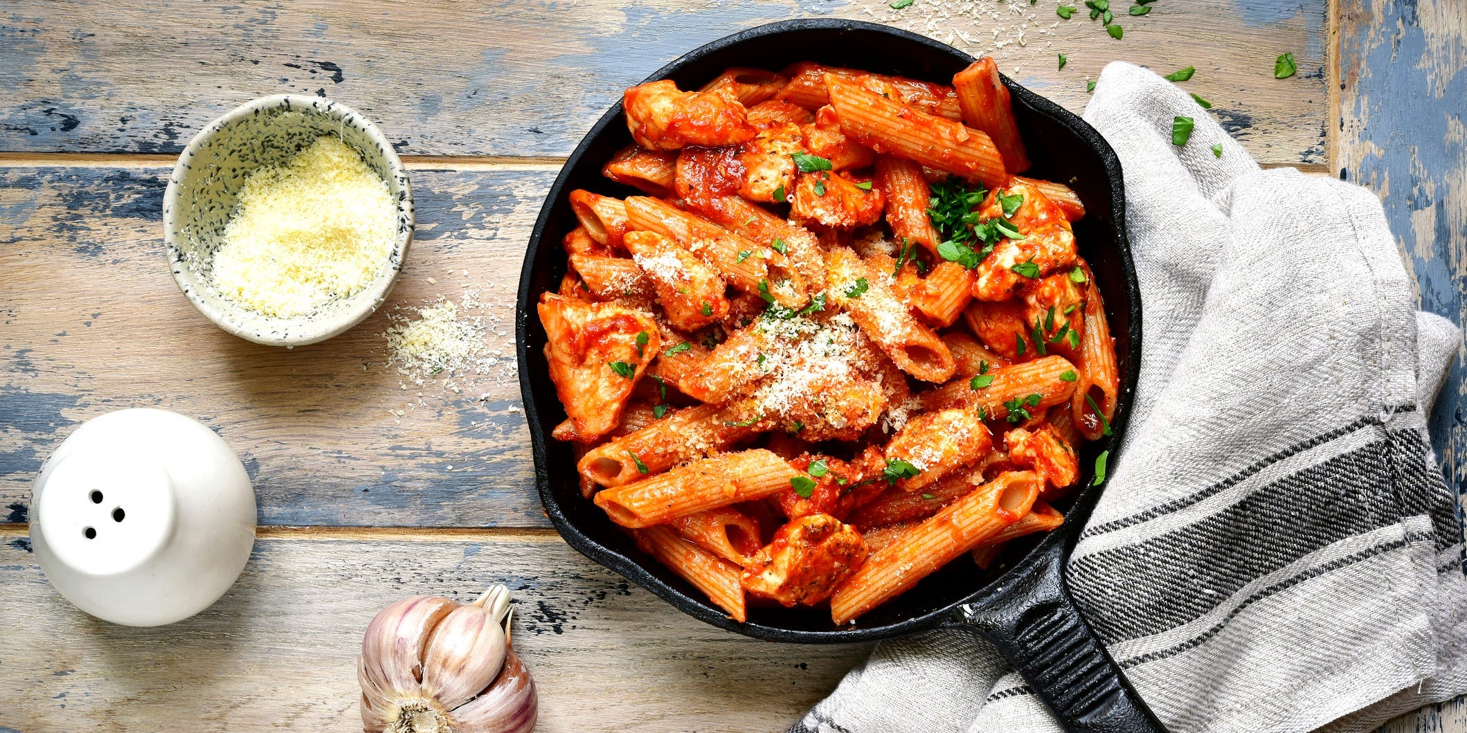 A cast iron skillet filled with whole wheat pasta, fresh garlic and herbs, and pasta sauce.