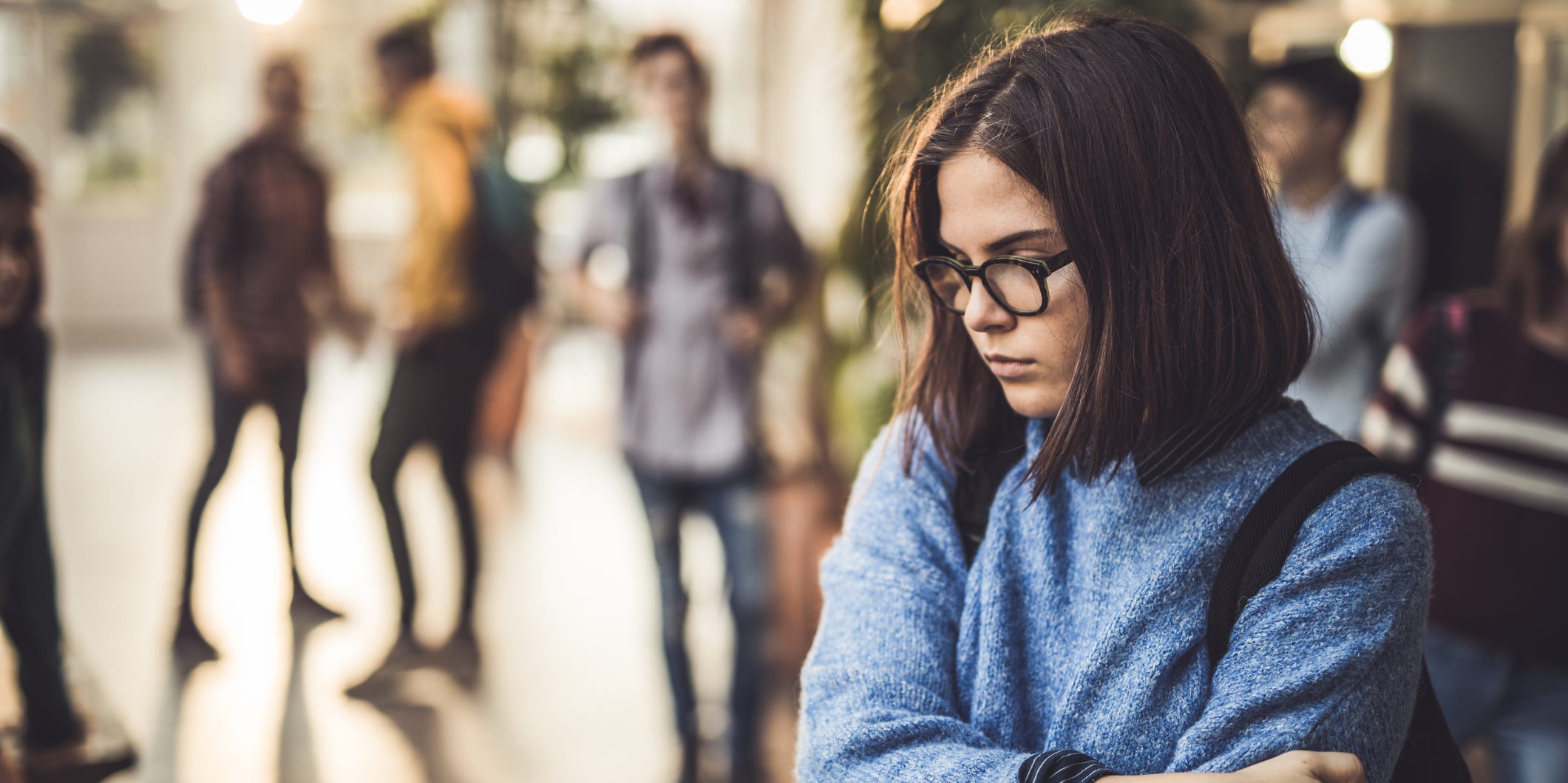 A girl stands alone away from a crowd of people.