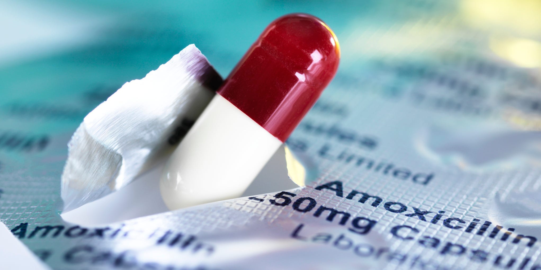 Close up of antibiotic Amoxicillin capsule popping out of foil, which reads "Amoxicillin 50mg Capsule."