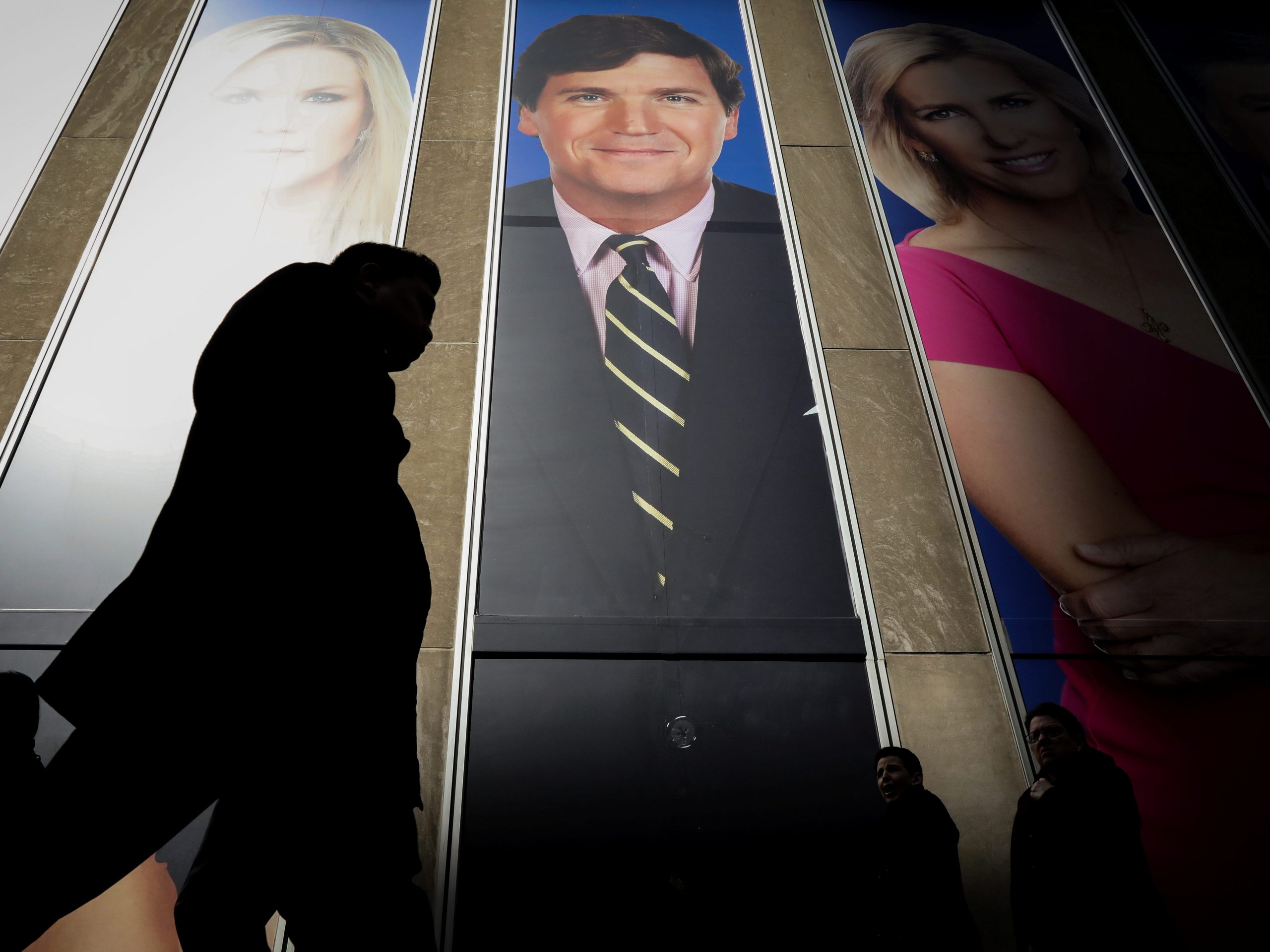 People pass by a promo of Fox News host Tucker Carlson on the News Corporation building in New York, US, March 13, 2019.
