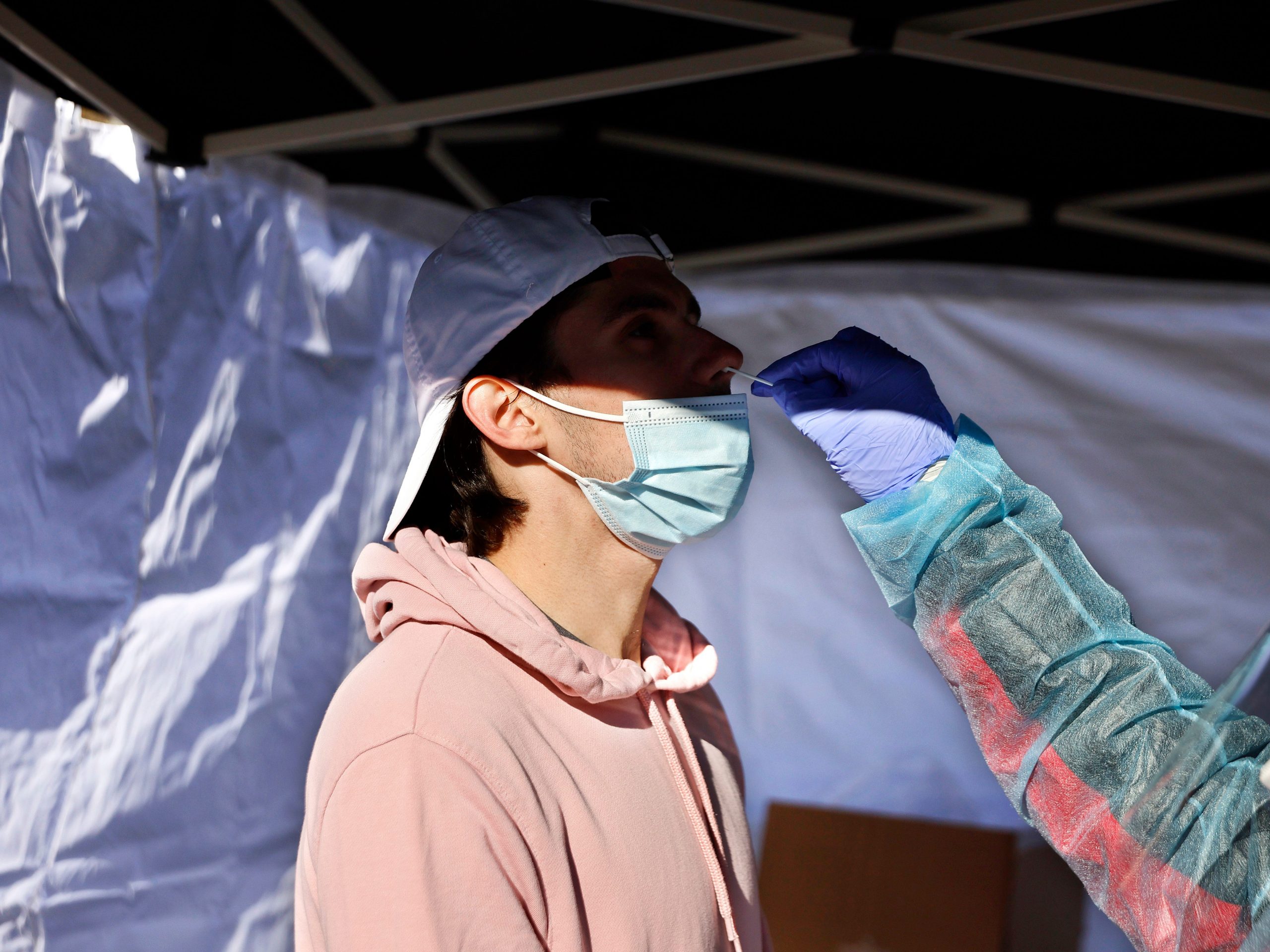 A person wearing white backwards cap and mask is tested for COVID-19.