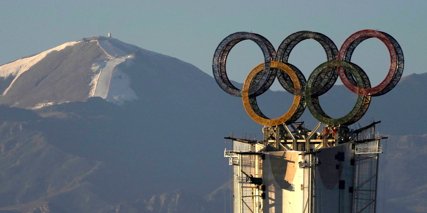 The Olympic rings sit atop a tower with mountains in the background near Beijing.