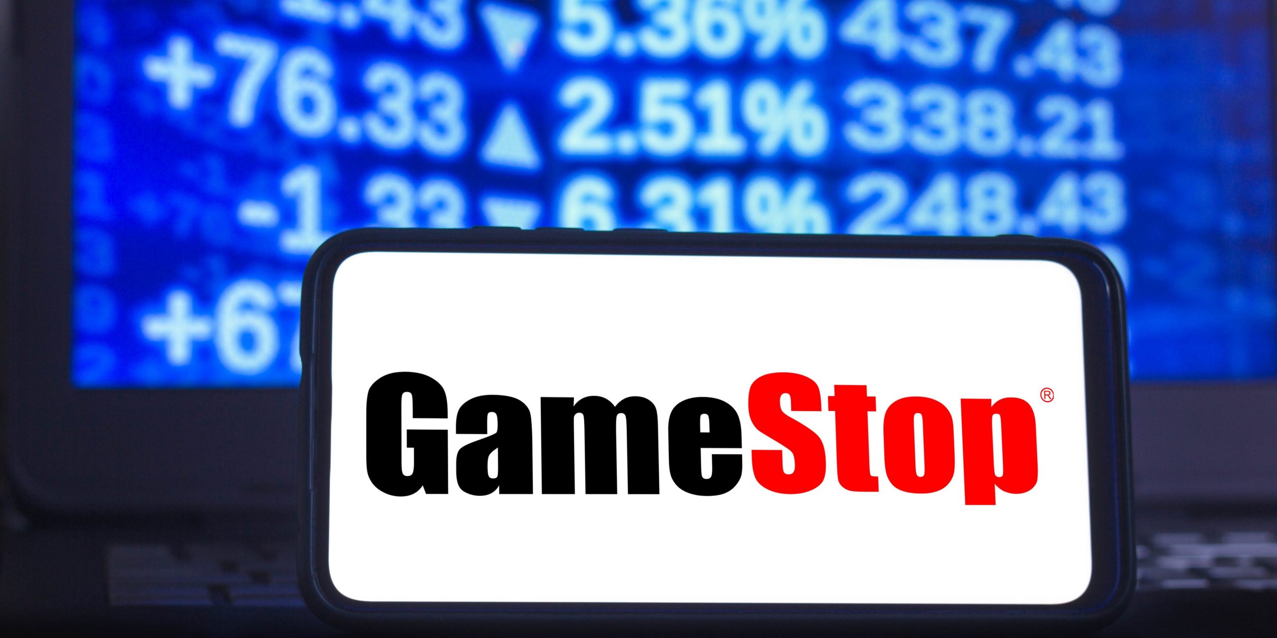 In this photo illustration a GameStop logo seen displayed on a smartphone with the stock market graphic in the background.