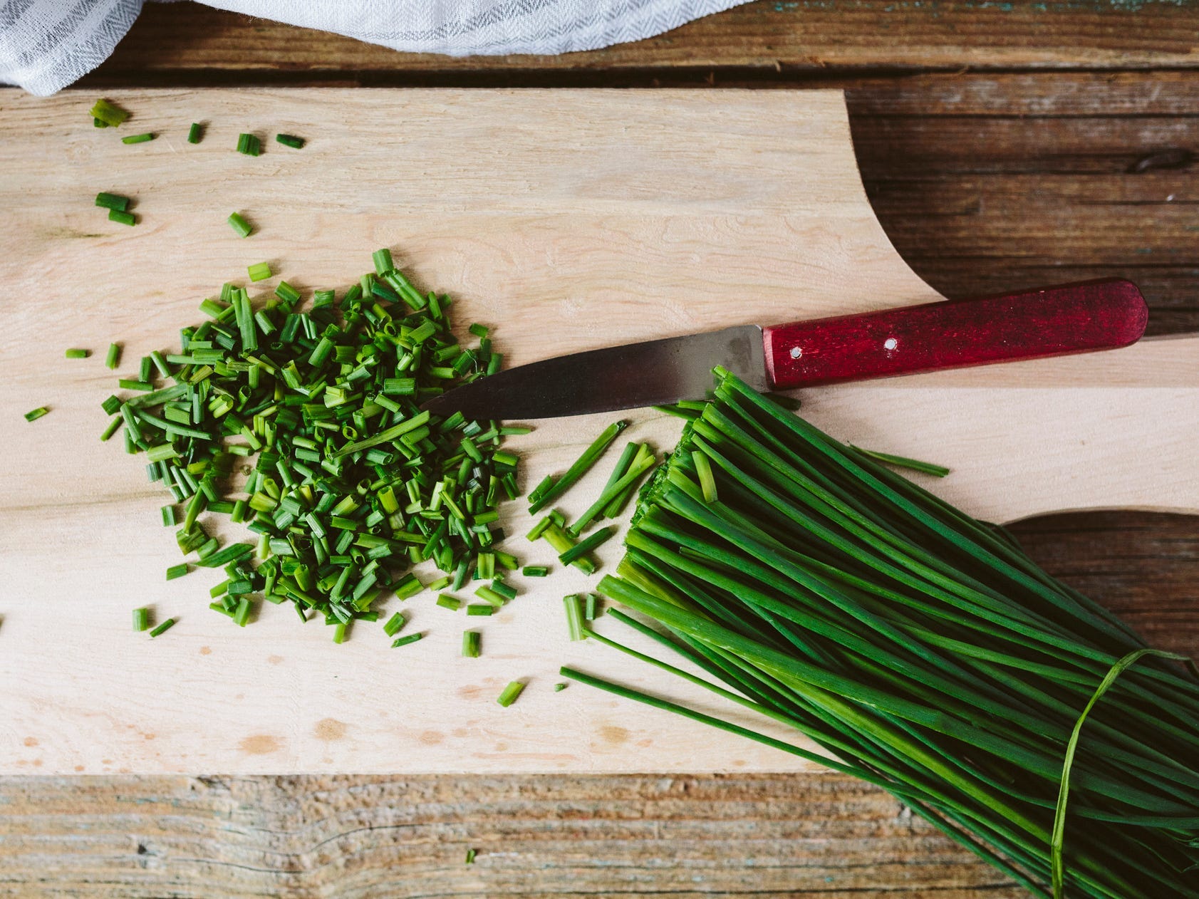 Whole and chopped chives on a wooden cutting board