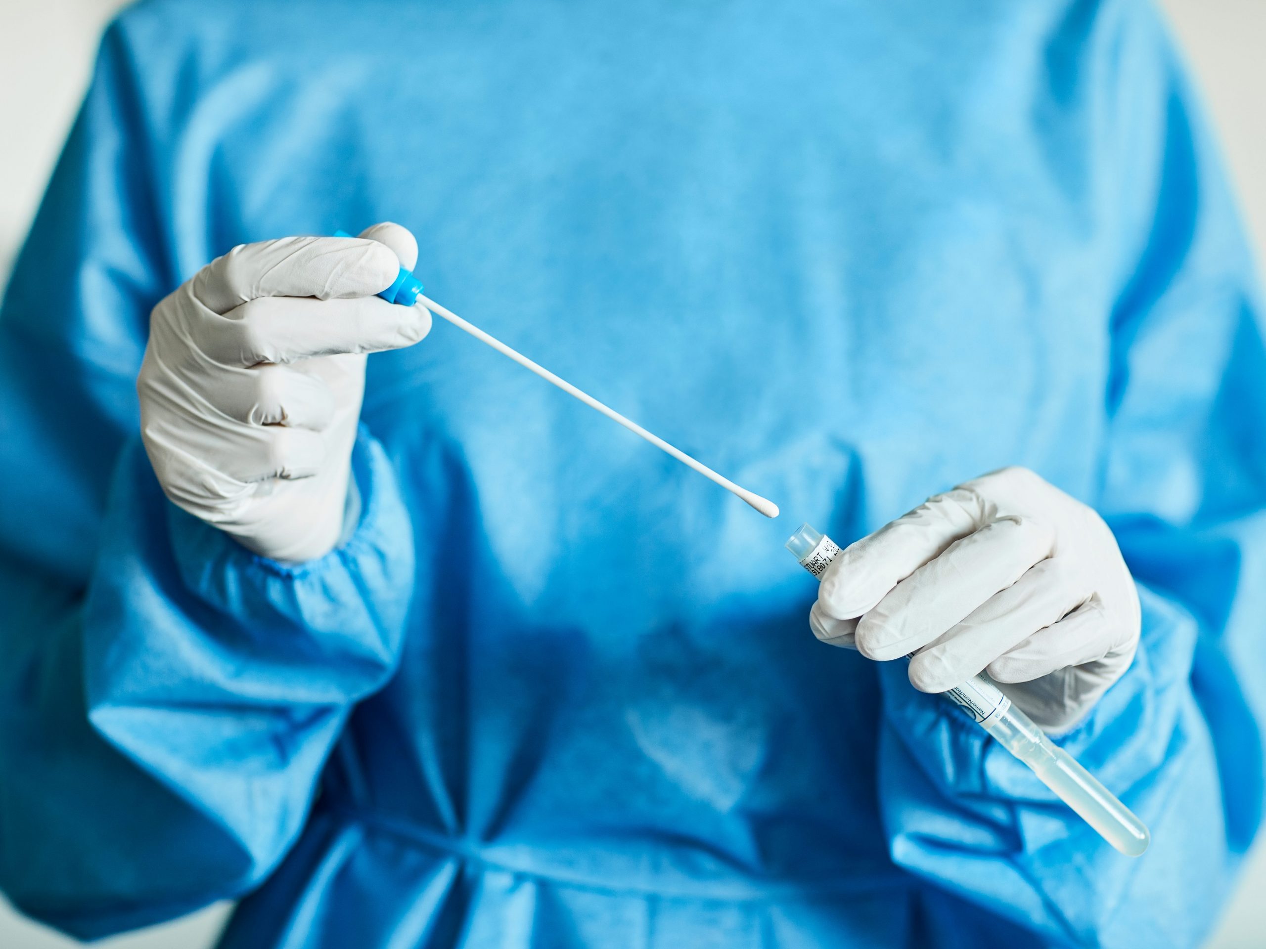 A posed picture of a person in PPE attire inserting a swab stick into a test tube.