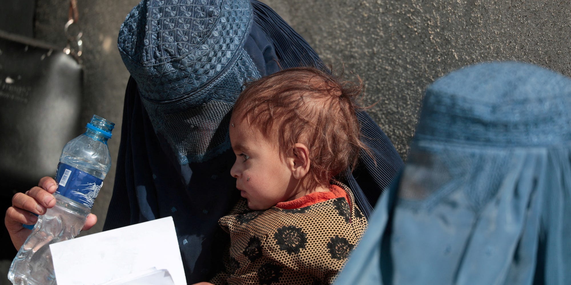 A displaced Afghan woman holds her child as she waits with other women to receive aid supply outside an UNCHR distribution center on the outskirts of Kabul, Afghanistan, in October 2021.