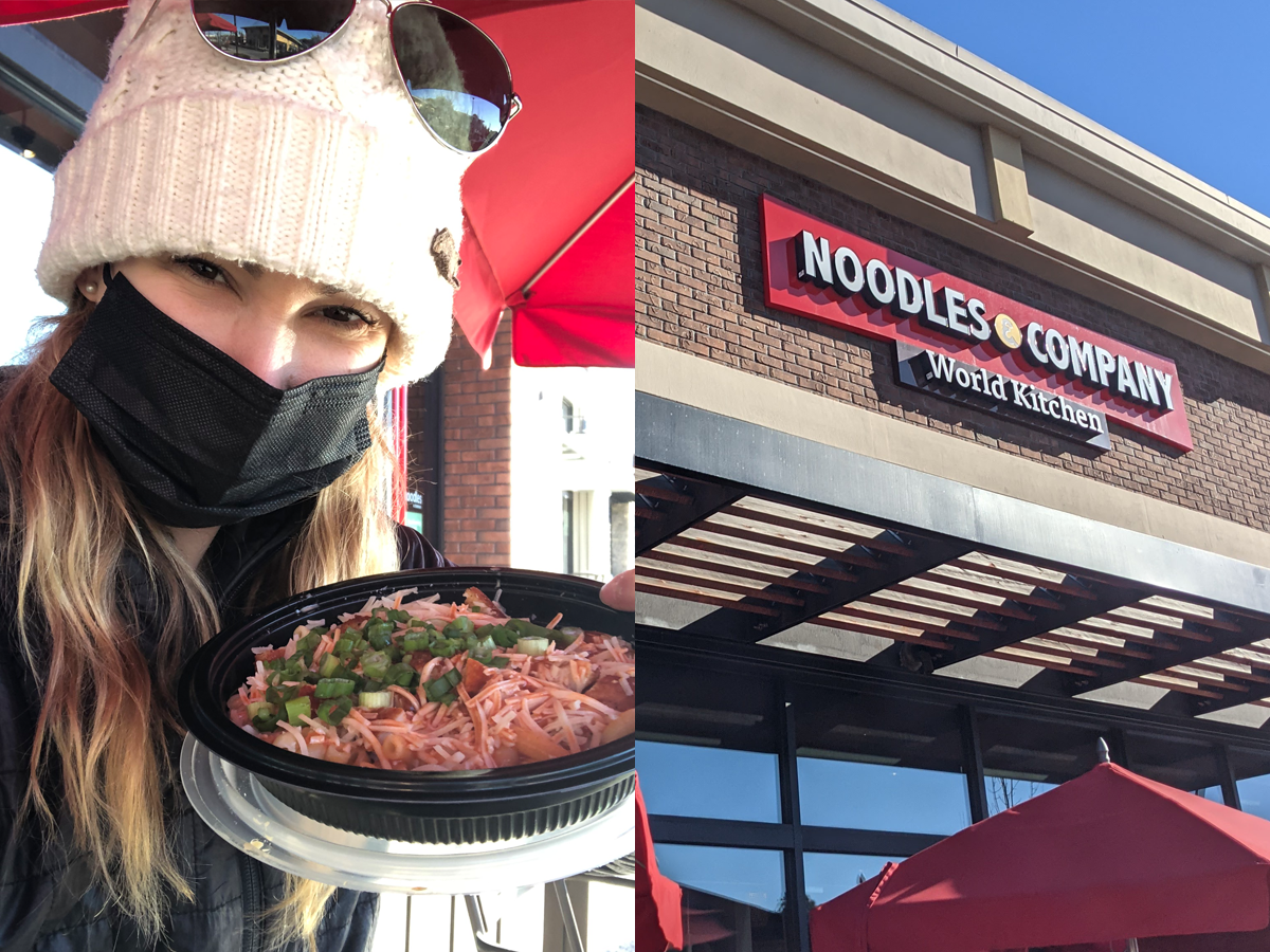 The writer holds a bowl of pasta and Noodles & Company sign