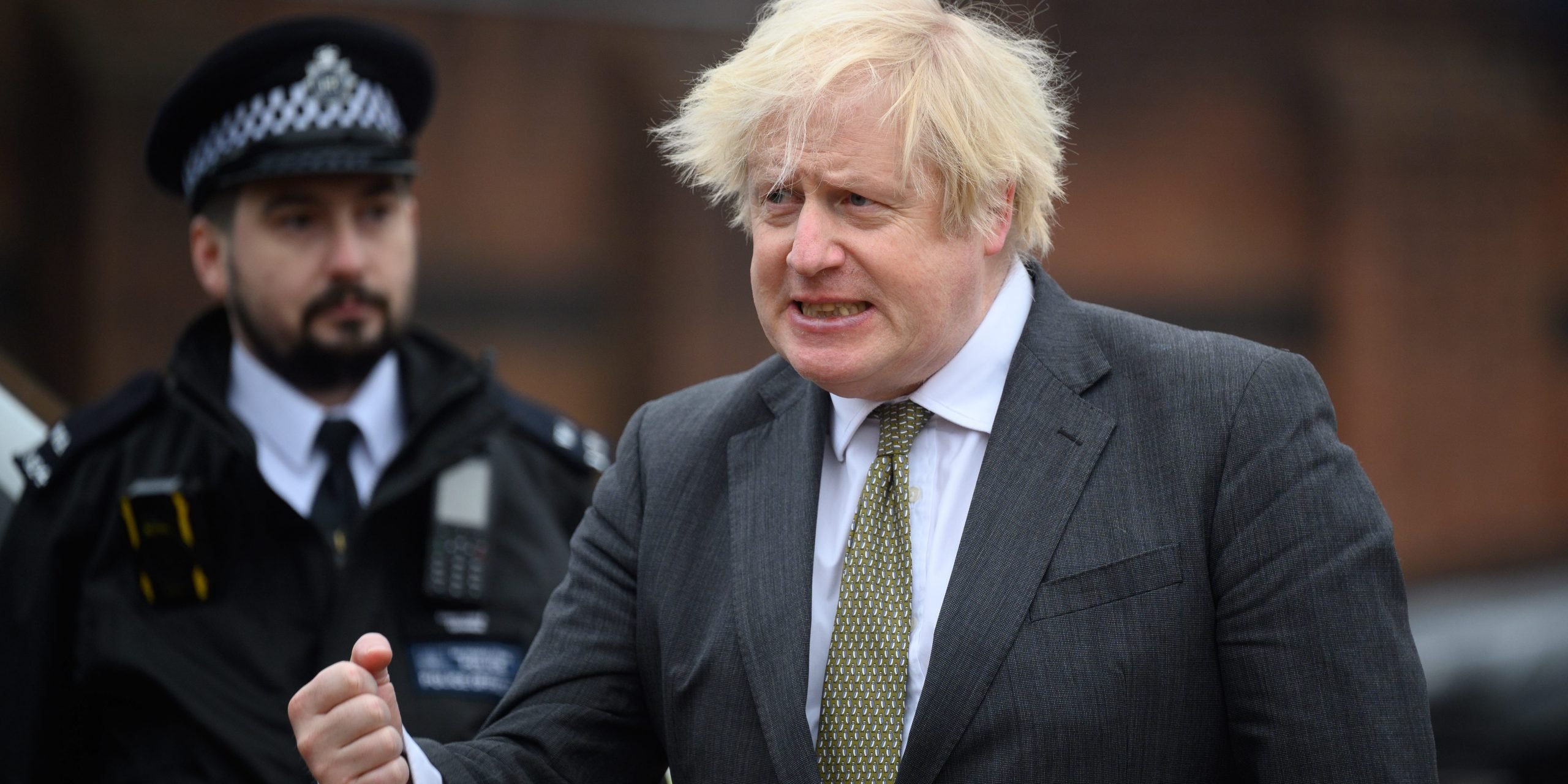 Boris Johnson at Uxbridge police station grimacing with an officer behind him