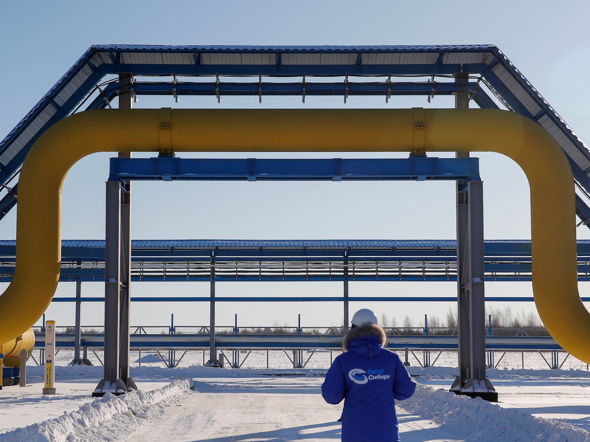 yellow gas pipeline above worker in blue jumpsuit in snow