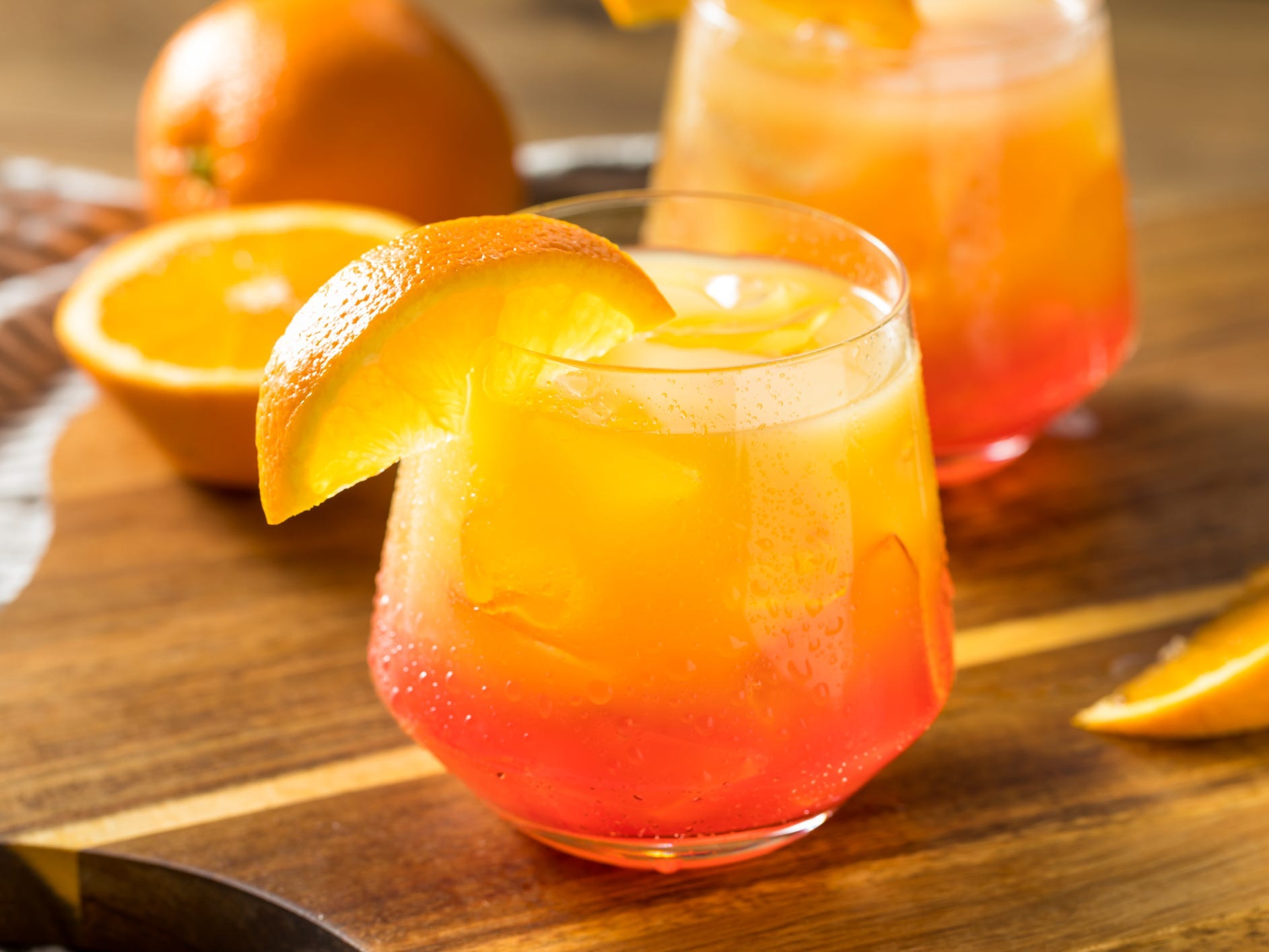A tequila sunrise in a short glass over ice, garnished with an orange wedge
