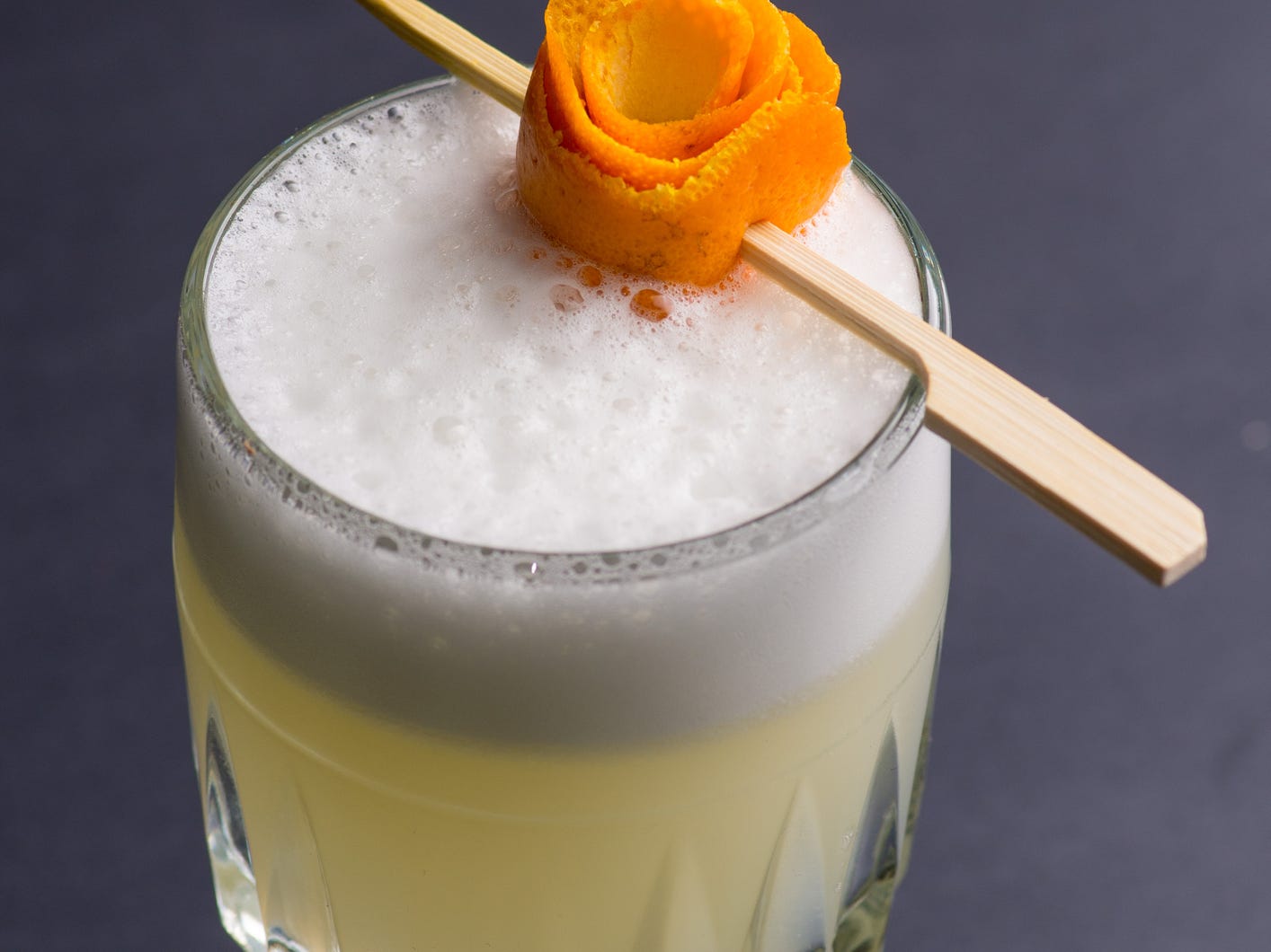 A white dragon cocktail with a head of egg white foam garnished with a skewered orange peel