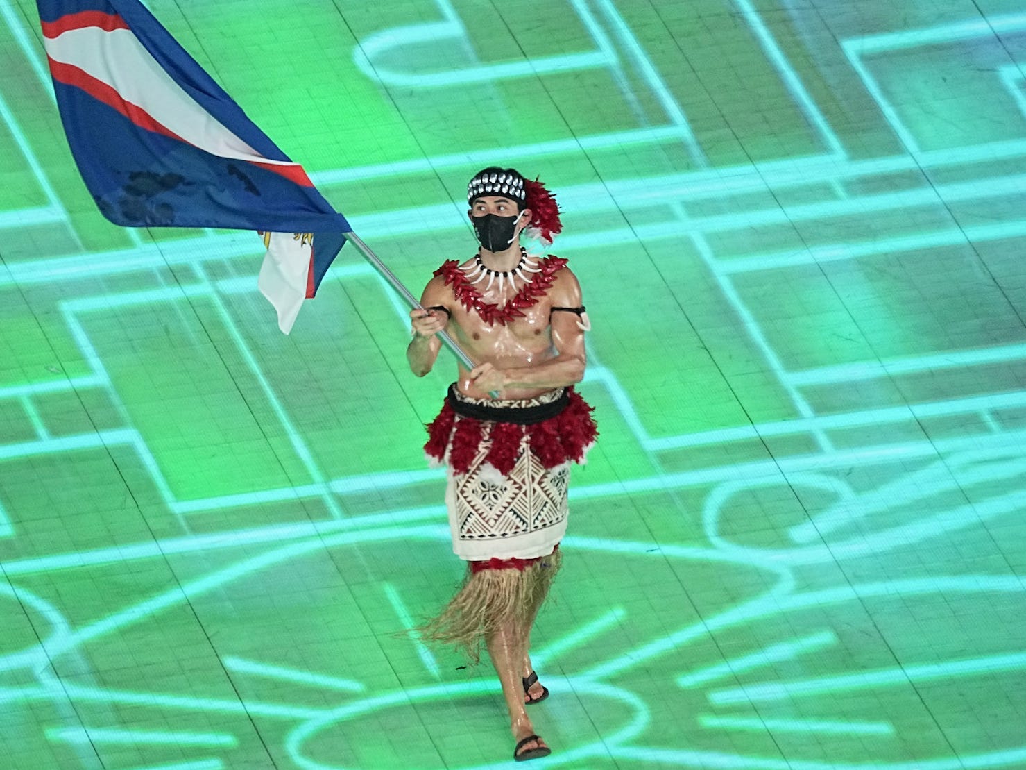 A shirtless Nathan Crumpton carries the American Samoa flag at the Olympic opening ceremony.