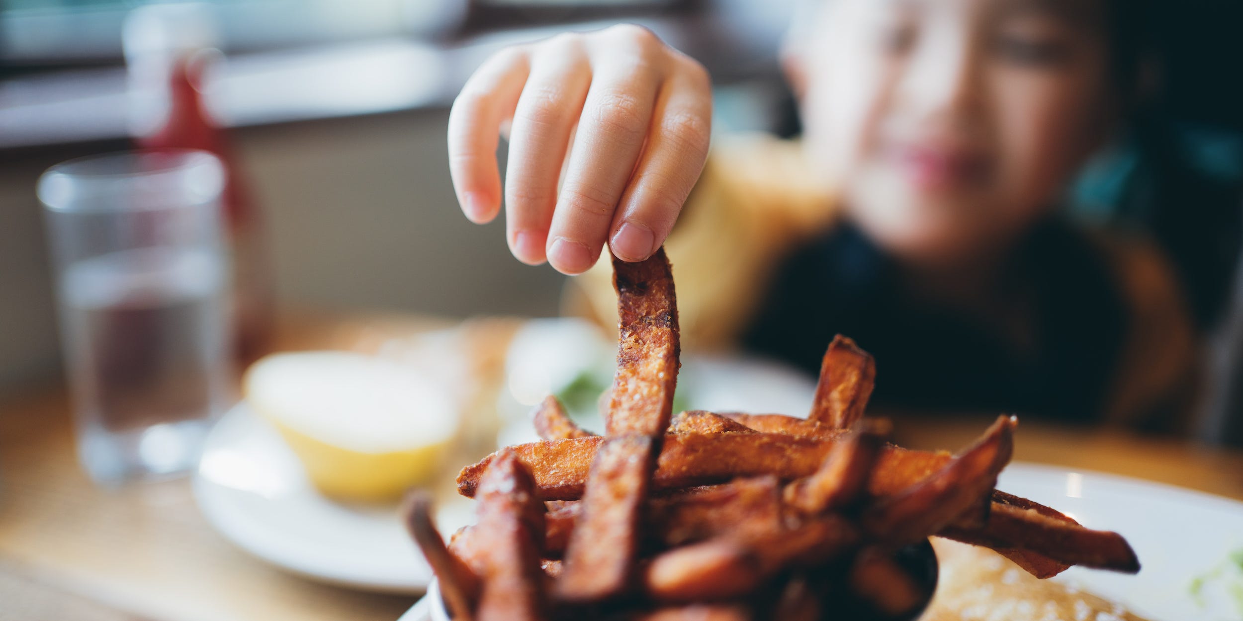 A young girl reaches across the table to grab a sweet potato fry.