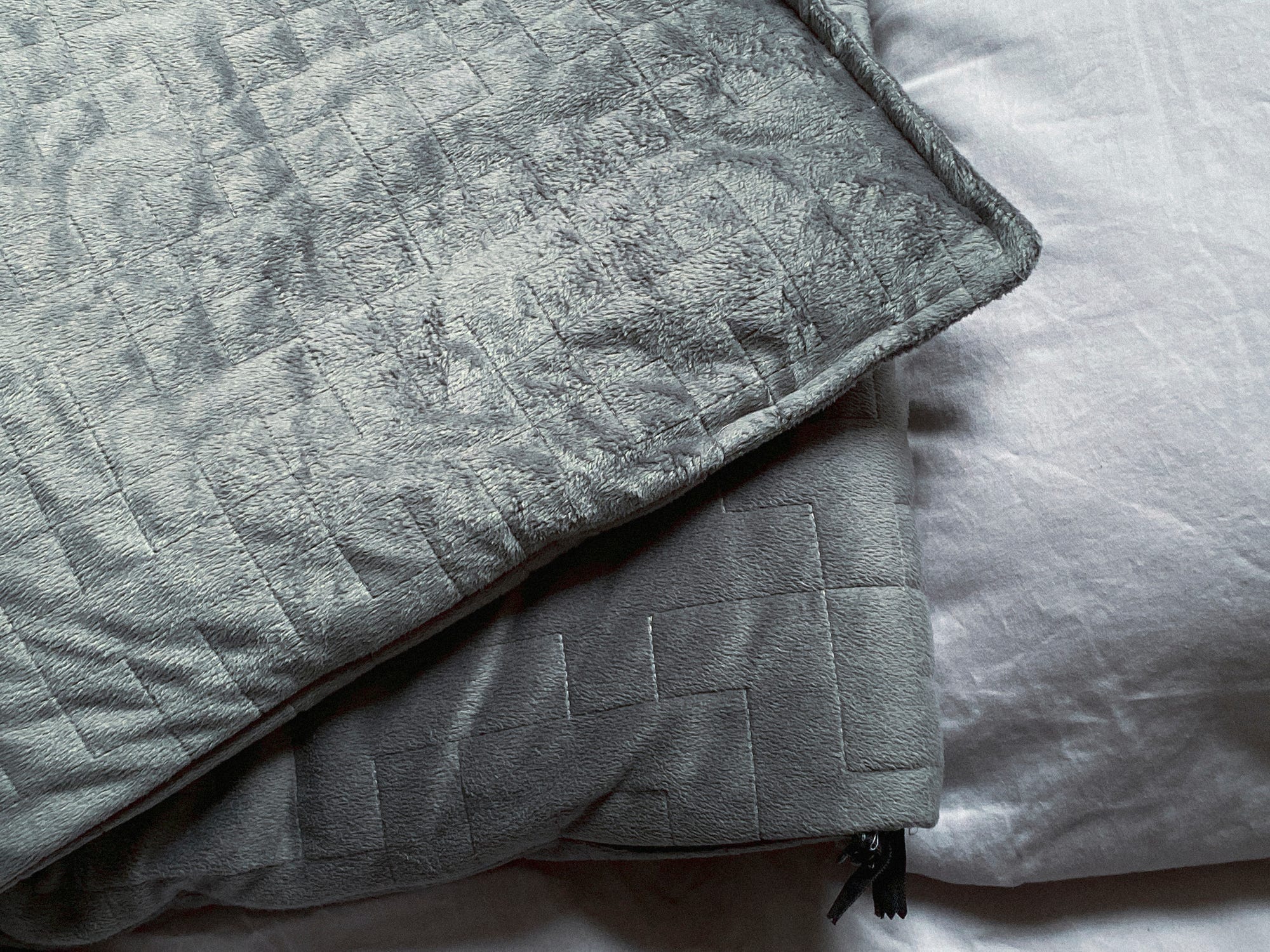 Close up of two corners of a weighted blanket on bedding