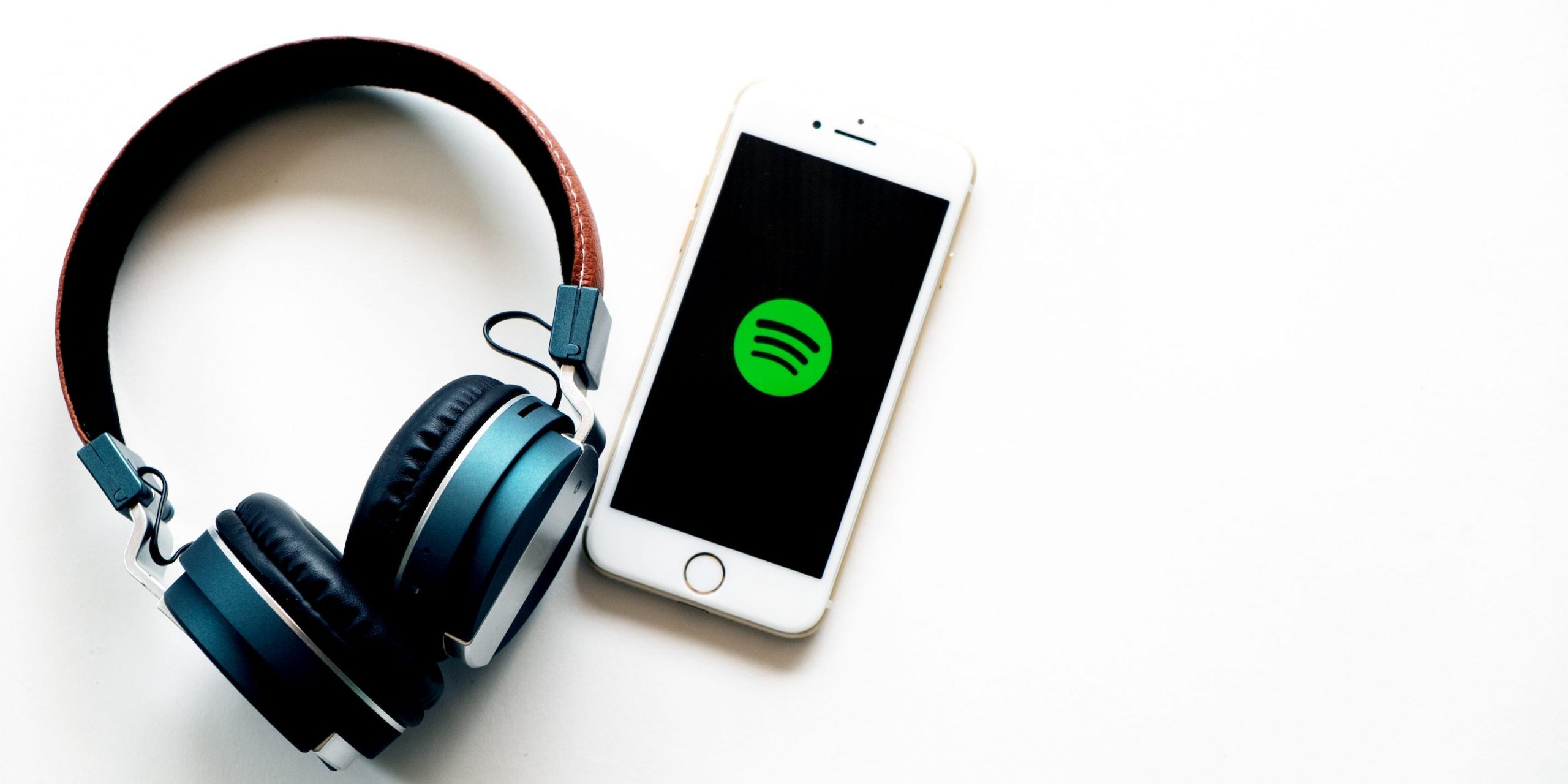 A pair of headphones laying next to a phone which displays the Spotify logo.