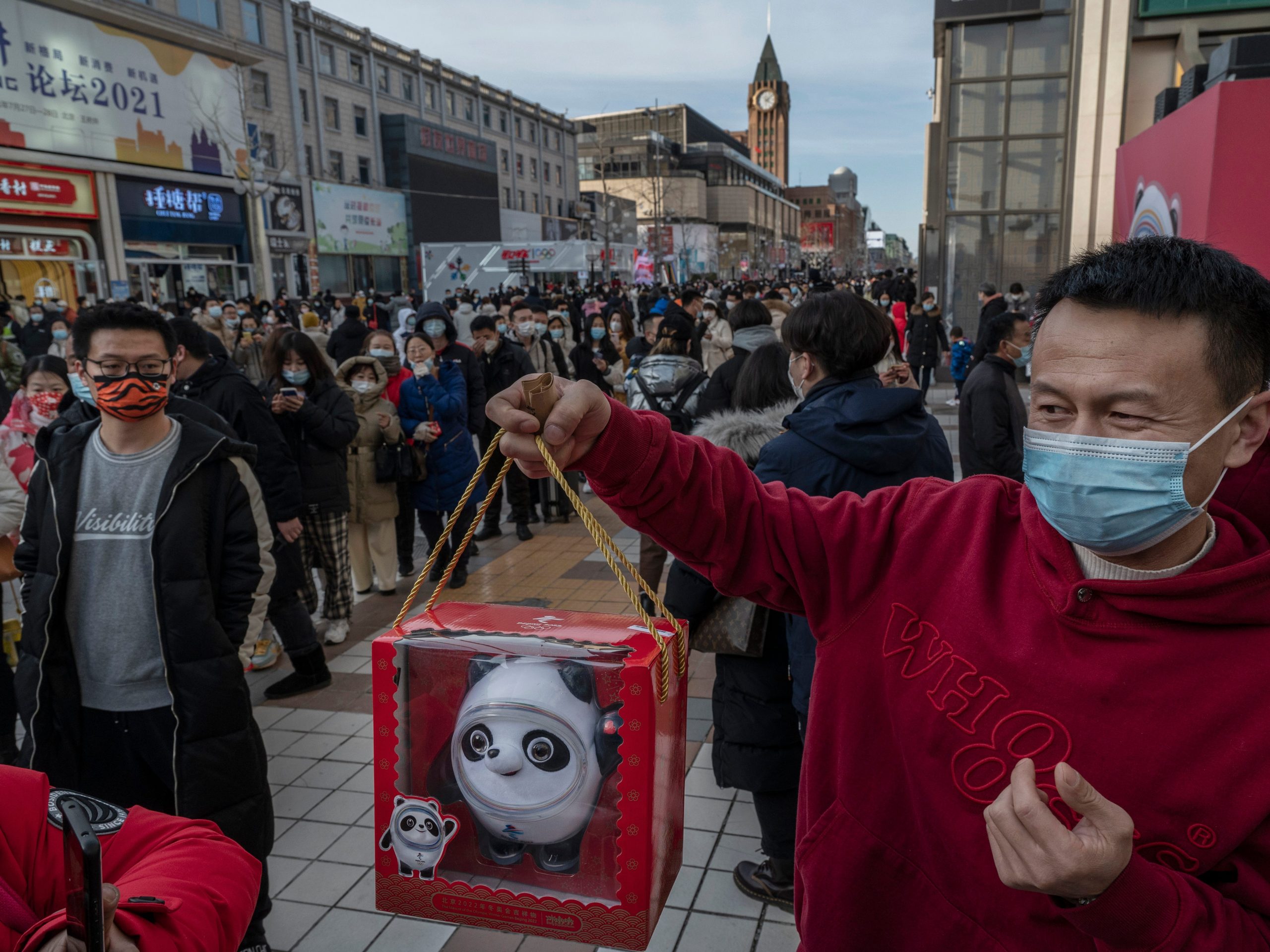 In China, a man holds a toy of mascot Bing Dwen Dwen he just bought as people line up with hundreds of others to enter the official Beijing 2022 Winter Olympics flagship store.