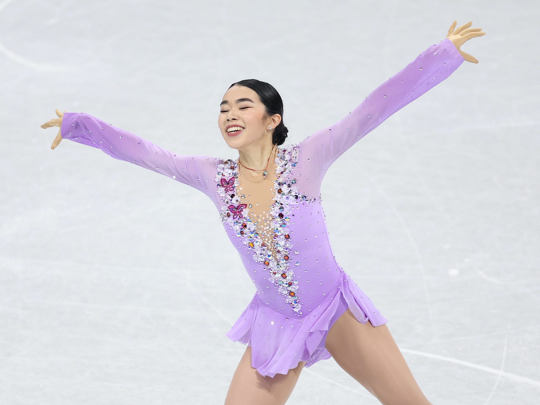 Karen Chen smiles and sweeps her arms out during a competition at the 2022 Winter Olympics.