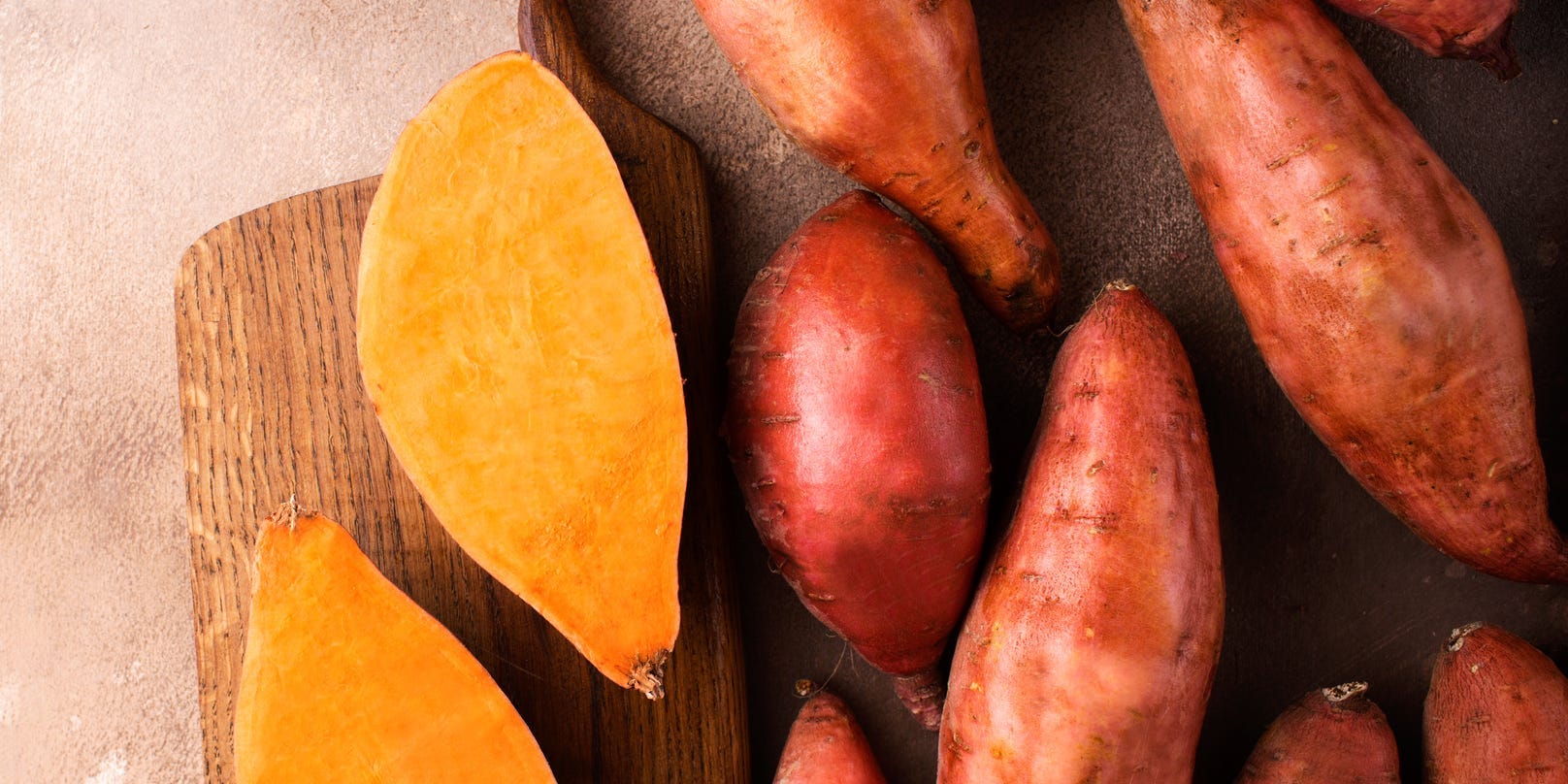 Sweet potatoes skewed to the right against a brown background. One is cut in half on a wooden board.