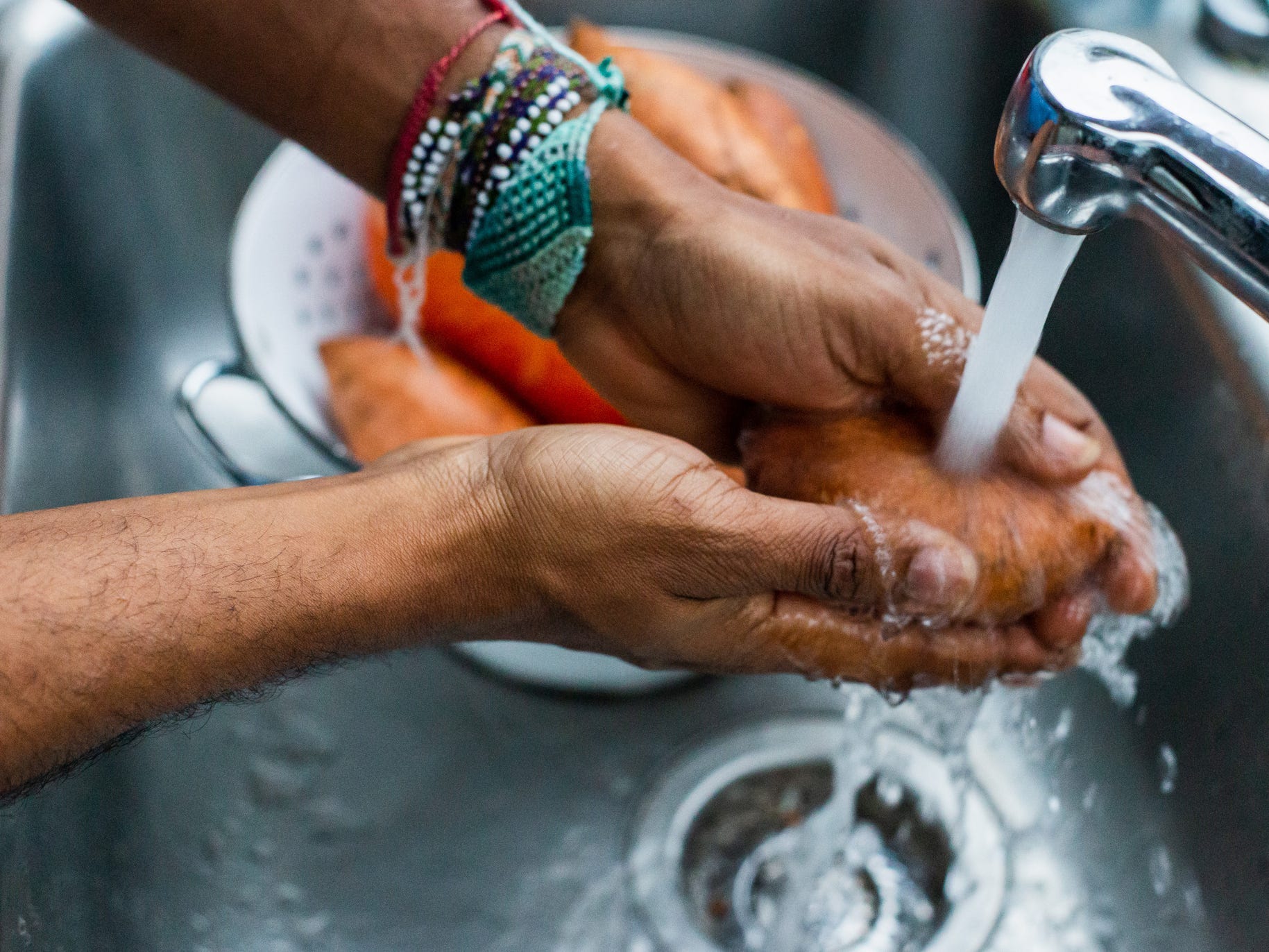 Person cleaning a sweet potato under running water