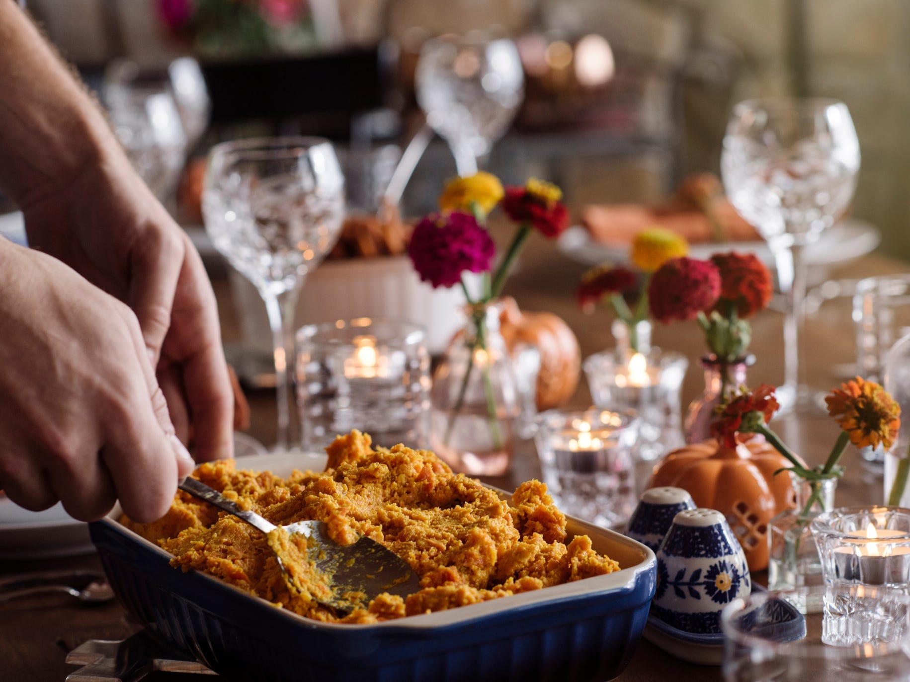 Person scooping sweet potato mash to serve at a well set dinner table