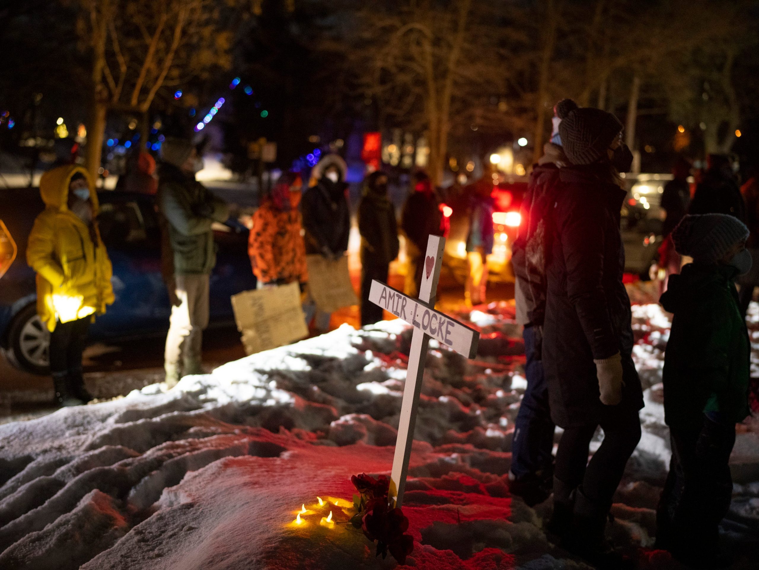 People stand by a cross planted in the boulevard outside homes at the intersection of and Dean Parkway and W. 28th St. in Minneapolis Sunday night.