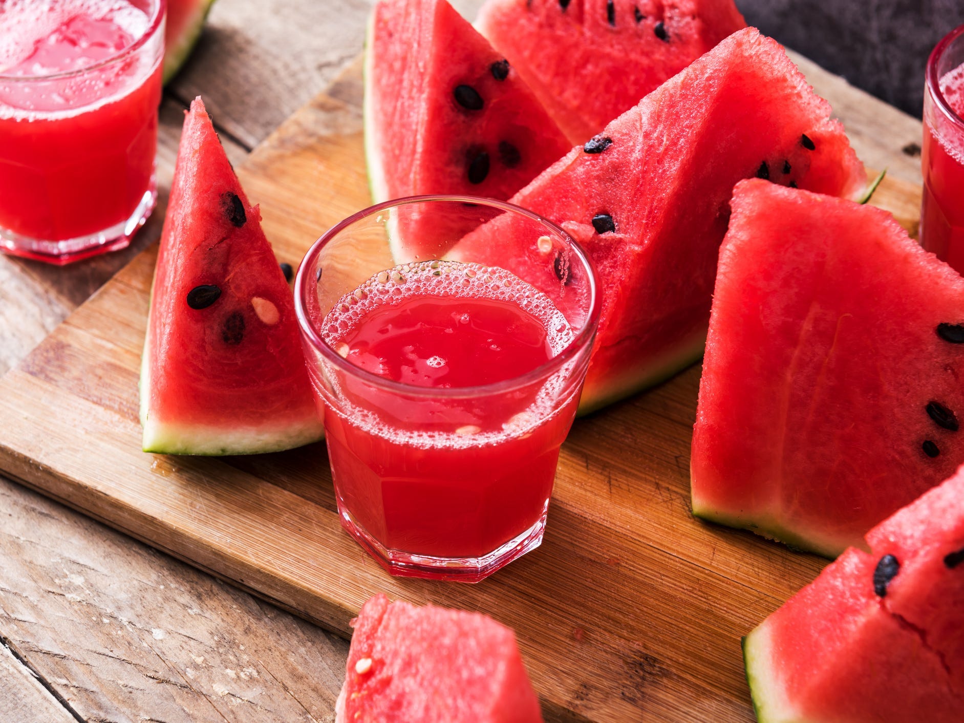 Watermelon slices and glasses of juice on a cutting board