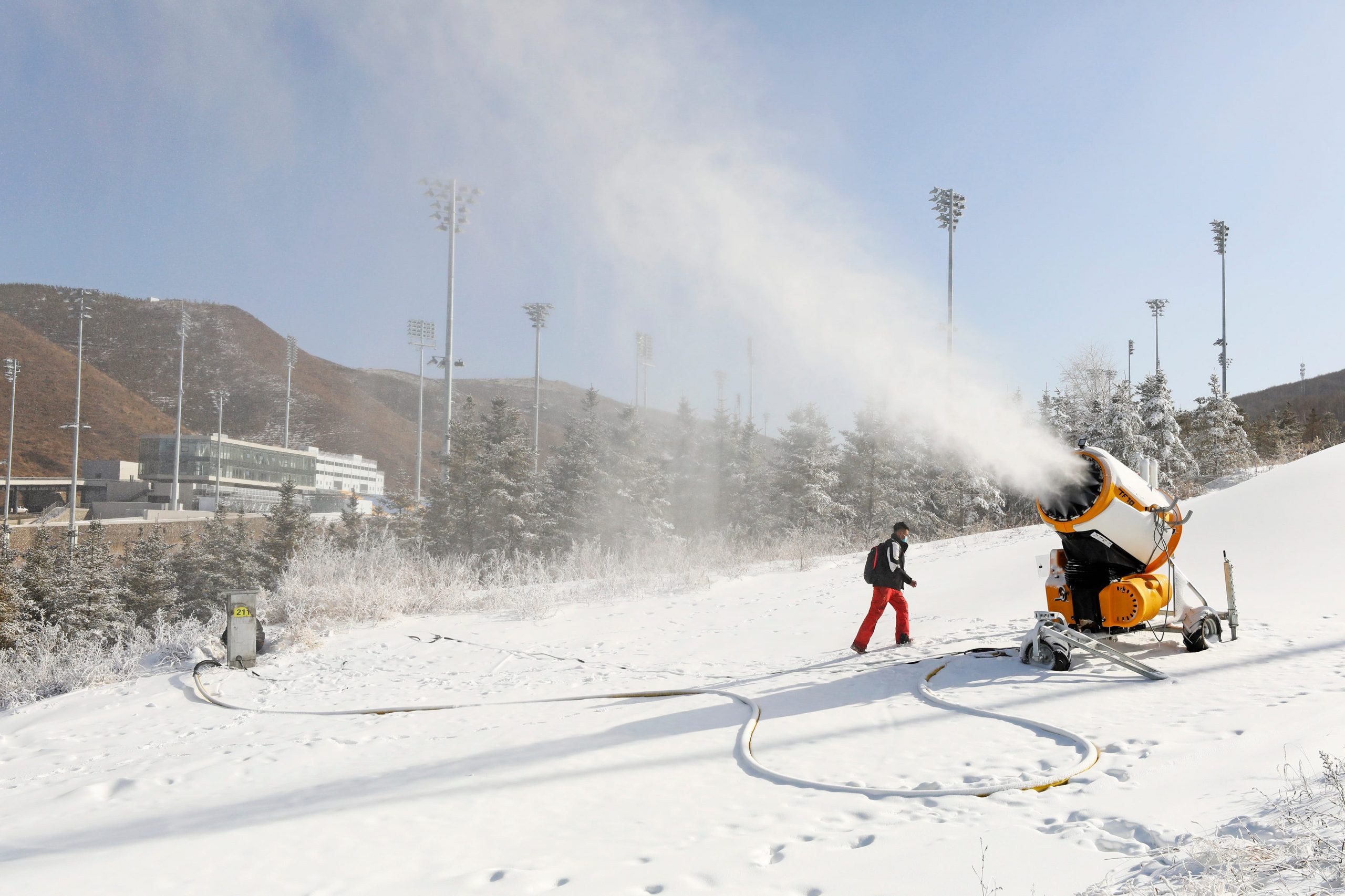 Snowmaking machine blows snow into the air as a worker stands near it